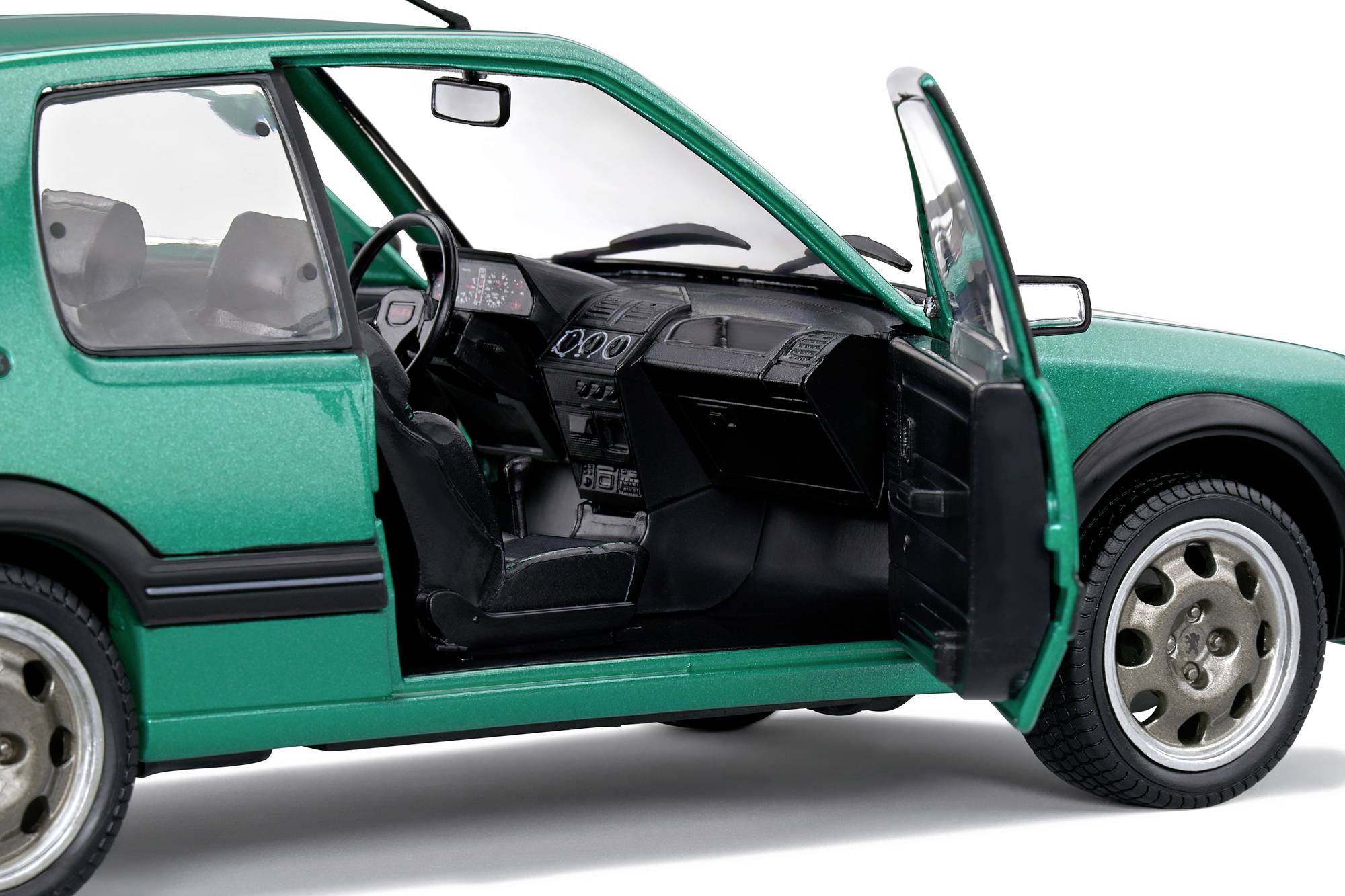 Grünes Auto mit offener Fahrertür, zeigt das schwarze Innenleben und Armaturenbrett. Das Fahrzeug steht still und ist fahrbereit.