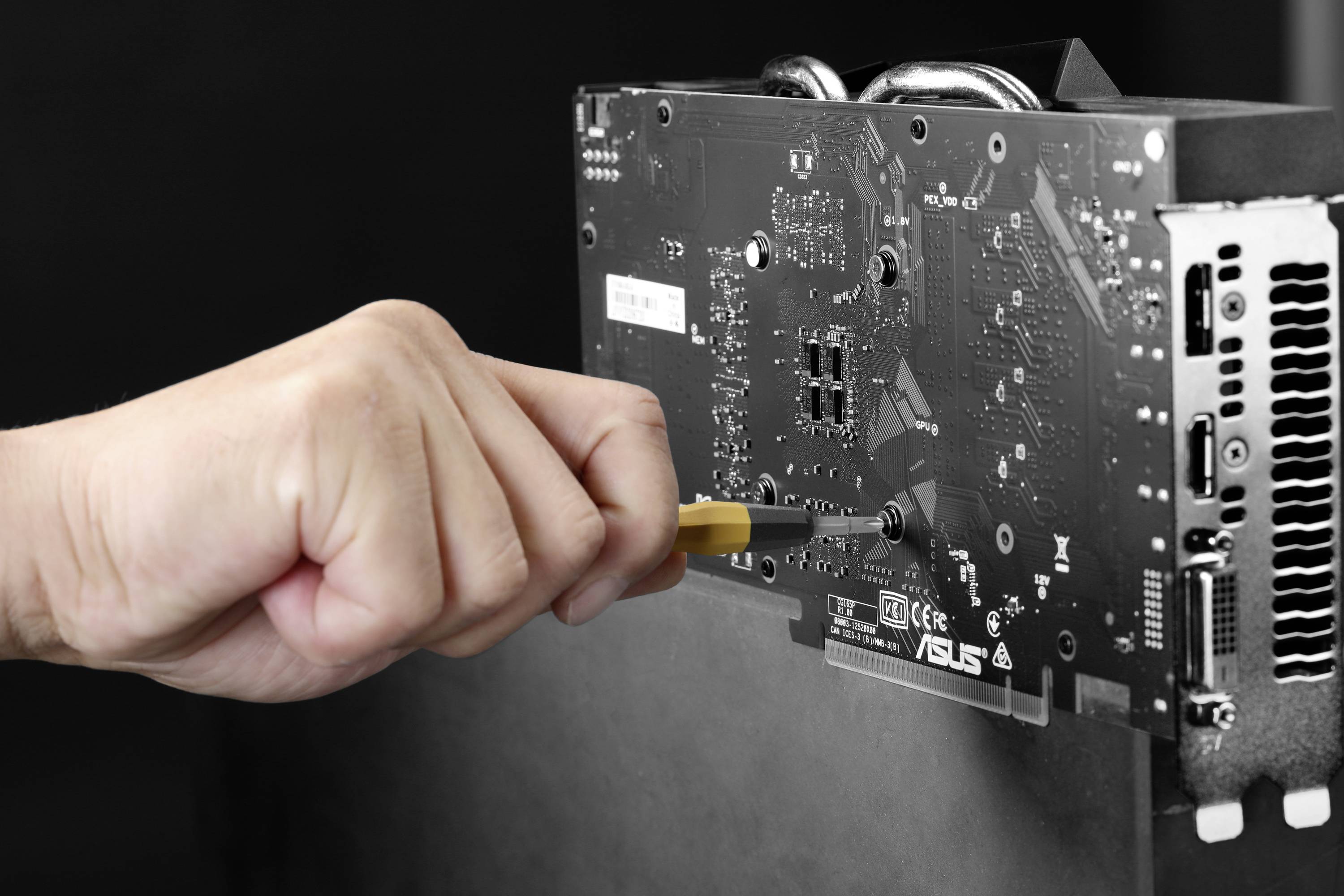 Eine Hand mit Schraubendreher befestigt eine Grafikkarte am Computergehäuse.