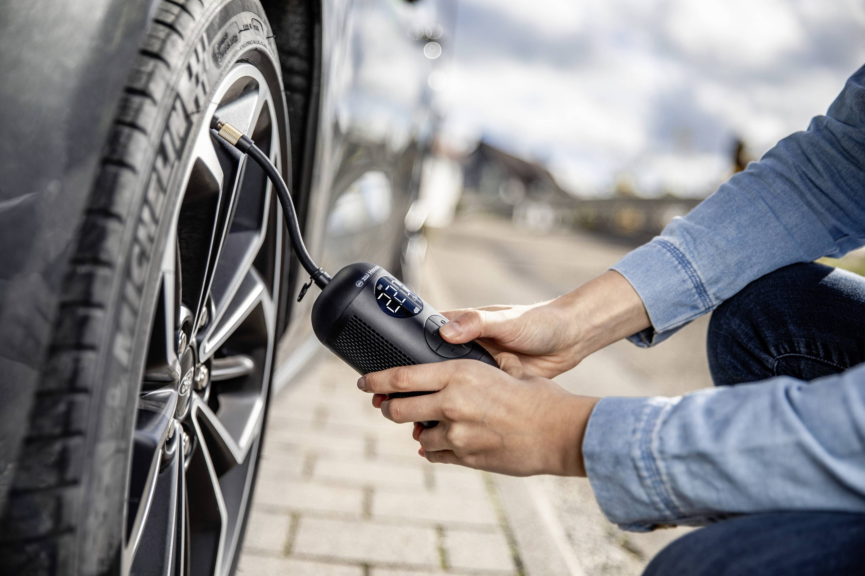 Eine Person pumpt an einem sonnigen Tag mit einer tragbaren Luftpumpe einen Reifen eines Autos auf einem Bürgersteig auf.