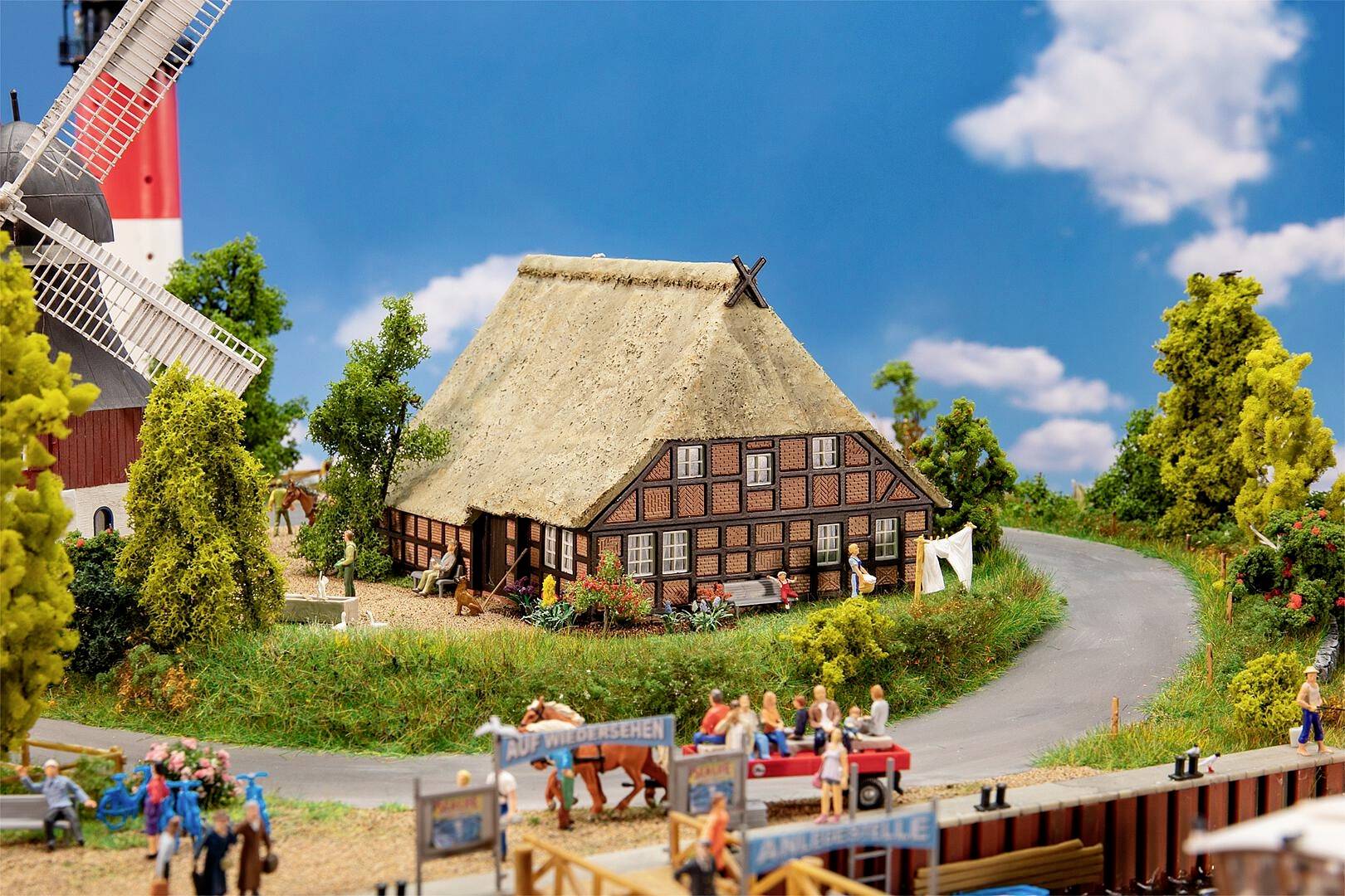 Ein Miniaturdorf mit einer Fachwerkhütte, umliegenden Bäumen und einer Windmühle; mehrere Figuren sind geschäftig auf dem Modellplatz.