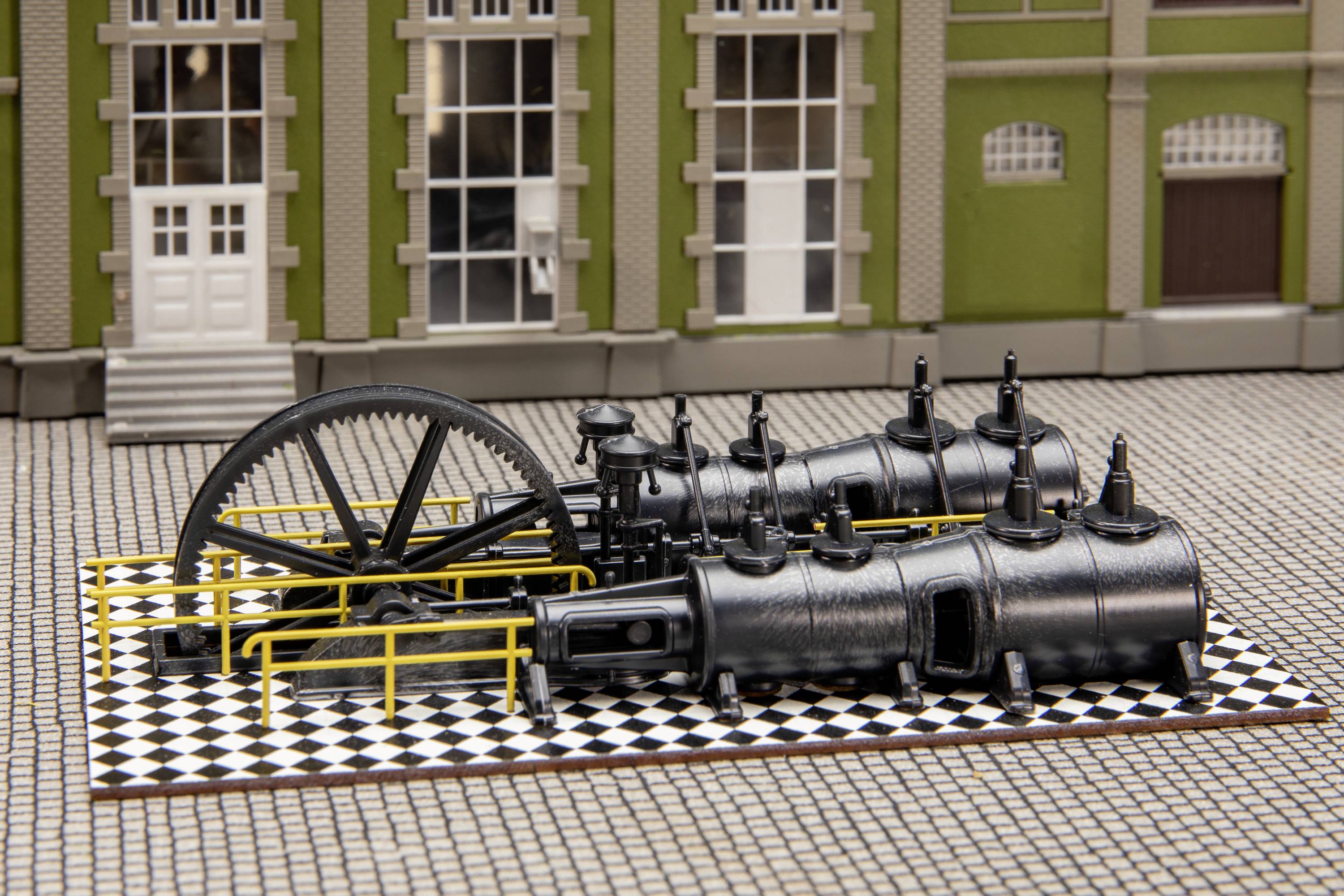 Ein Modell einer alten Dampfmaschine mit großen schwarz lackierten Zylindern und Rädern, auf einem Schachbrettmuster platziert.