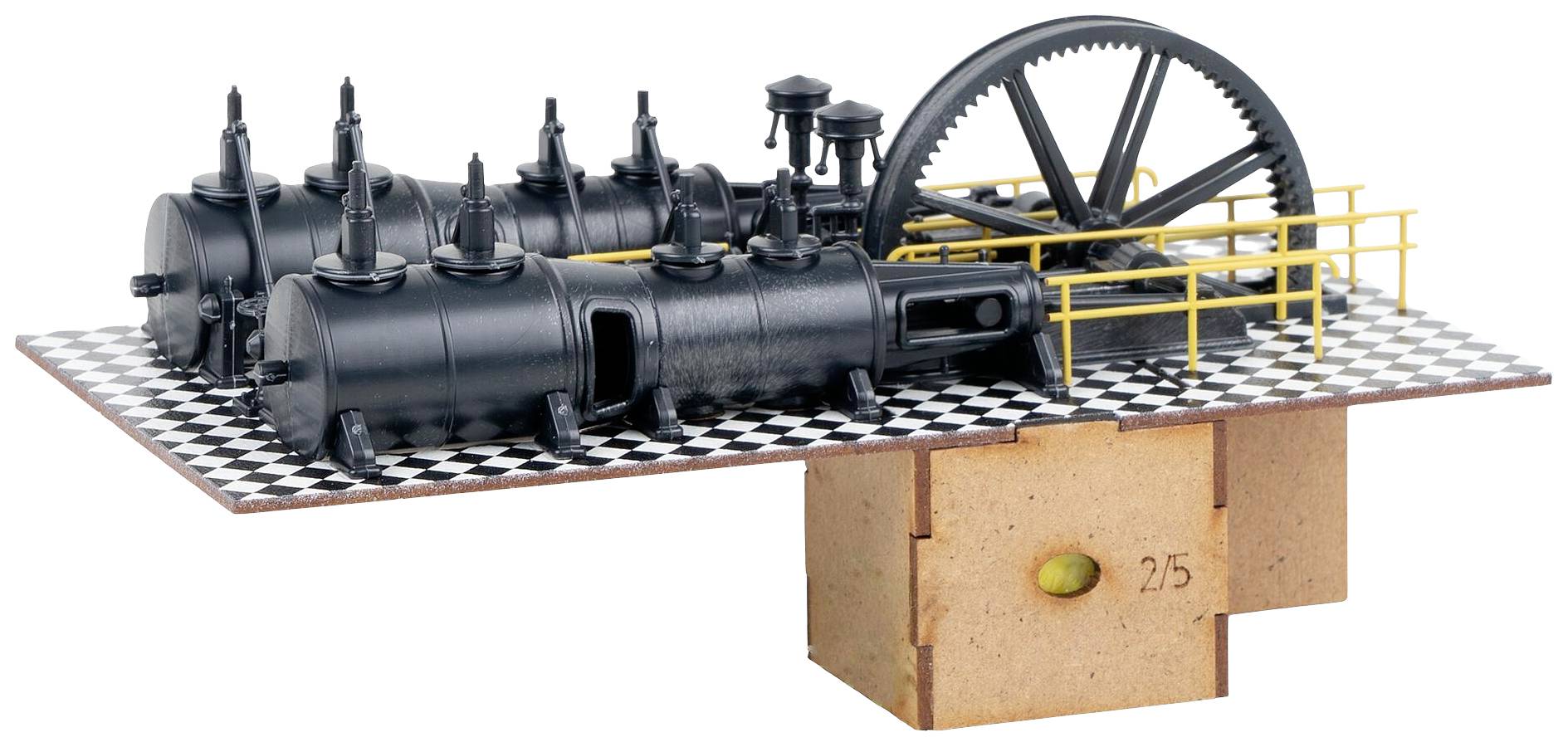Ein Modell einer Dampfmaschine auf einer karierten Plattform mit gelben Geländern. Die Maschine hat mehrere schwarze Zylinder und ein großes Zahnrad.
