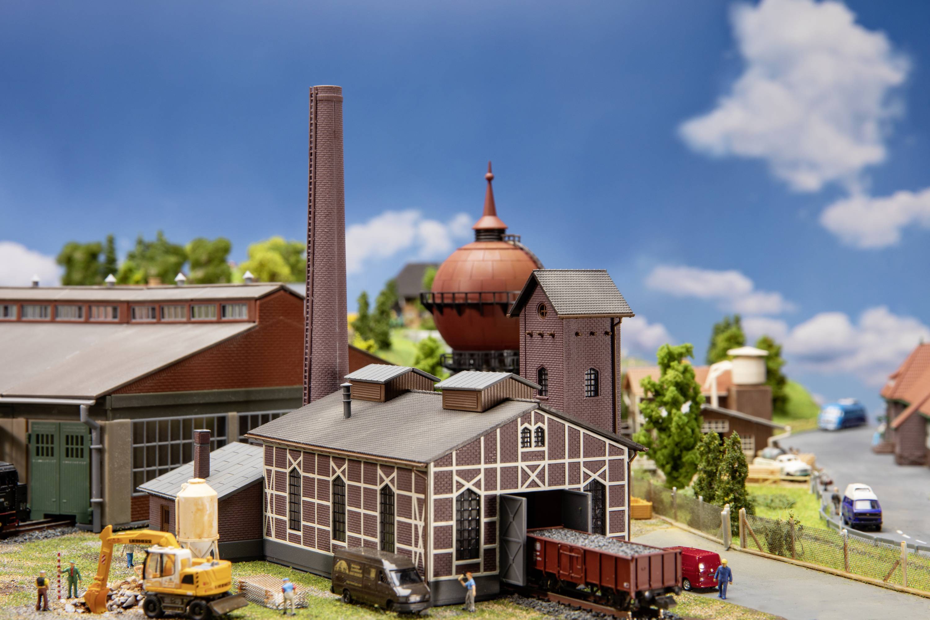 Miniatur Eisenbahnanlage mit Gebäuden, Schienen und Zügen. Detaillierte Architektur und Landschaftsgestaltung. Blauer Himmel im Hintergrund.