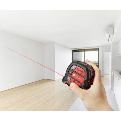 Person misst mit einem Laser-Entfernungsmesser den Raum einer modernen, leeren Wohnung mit Holzboden.