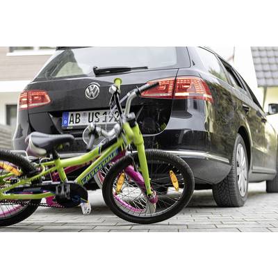 'Ein Fahrrad liegt auf dem Bürgersteig hinter einem geparkten Auto. Das Fahrrad ist bunt und das Auto ist schwarz.'