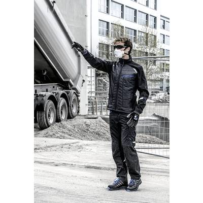 Eine Person in Arbeitskleidung und Maske zeigt auf eine Baustelle. Ein Lastwagen steht im Hintergrund. Gebäude und Bauzäune sind sichtbar.
