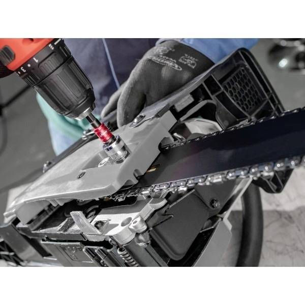 Eine Person mit Handschuhen benutzt einen roten Bohrer an einem mechanischen Teil einer Motorsäge, möglicherweise bei Wartungs- oder Montagearbeiten.