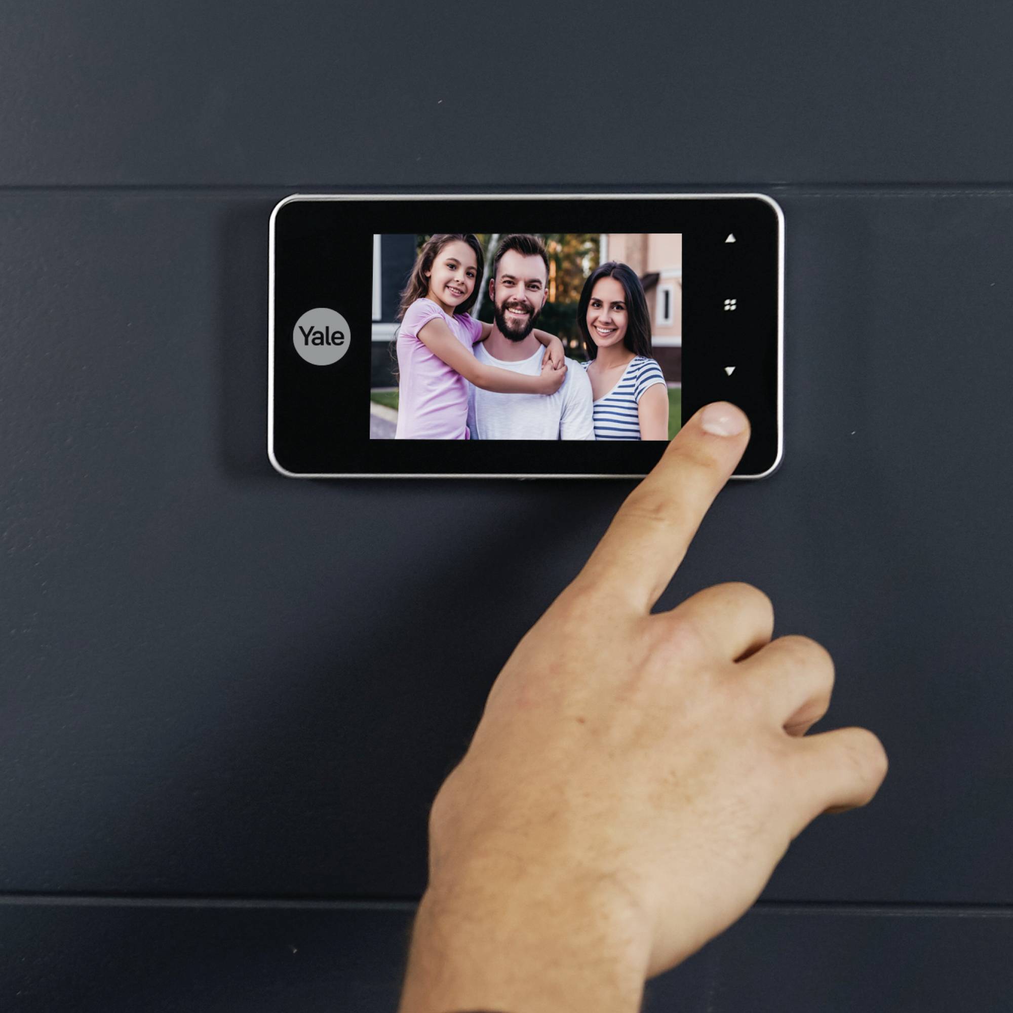 Eine Person berührt ein Smart-Gerät an der Wand, auf dem ein Familienfoto mit zwei Erwachsenen und einem Kind angezeigt wird.