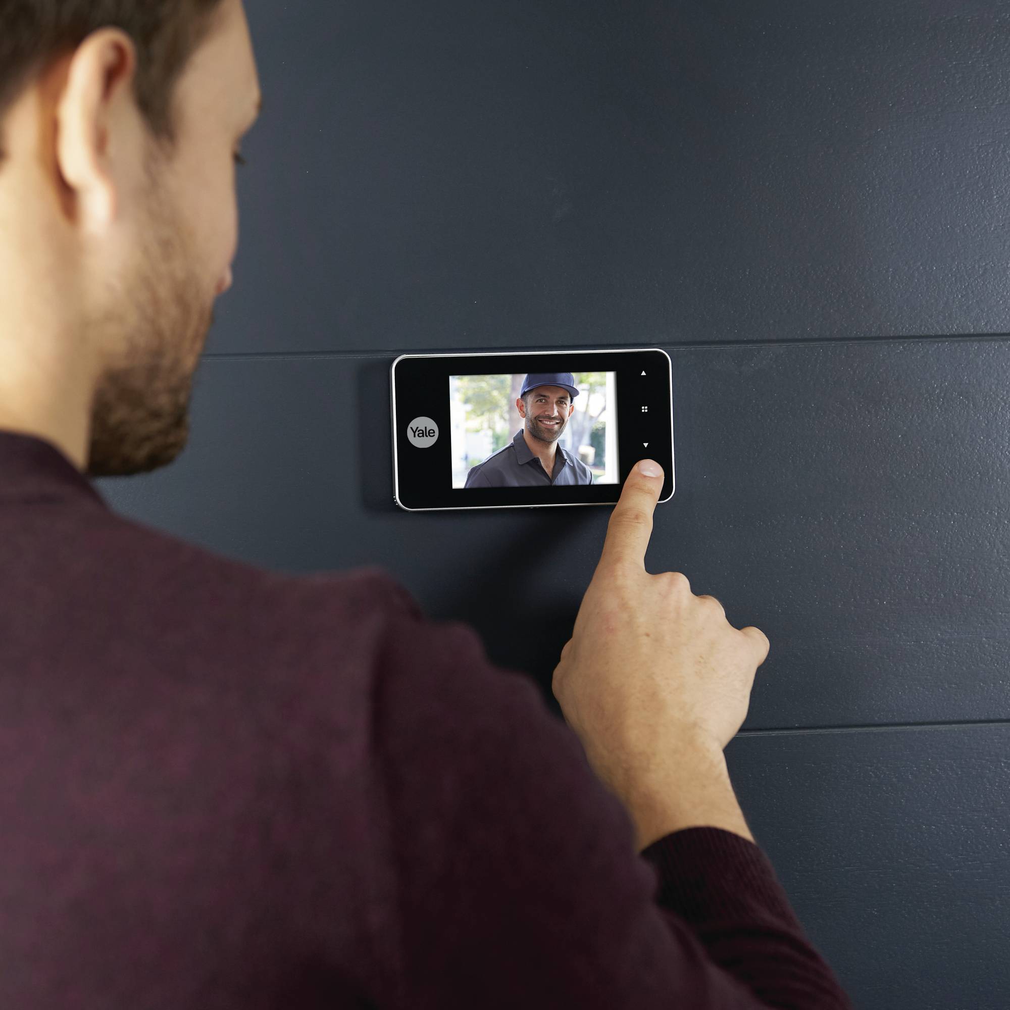 Eine Person betrachtet ein Display mit dem Bild eines lächelnden Mannes, der auf einem Bildschirm an einer blauen Wand erscheint.