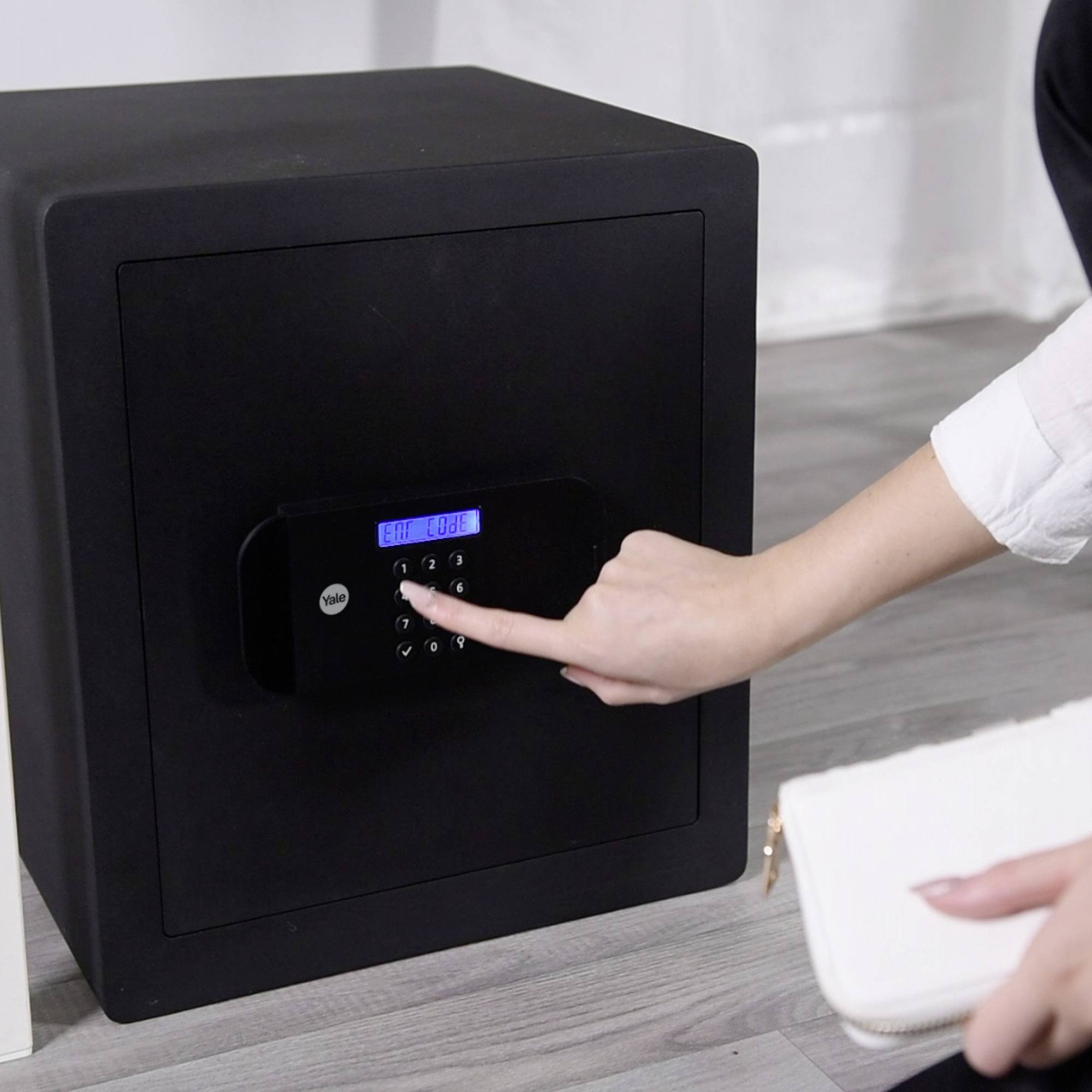 Eine Person tippt eine Zahlenkombination in ein elektronisches Schloss an einem schwarzen Tresor ein.