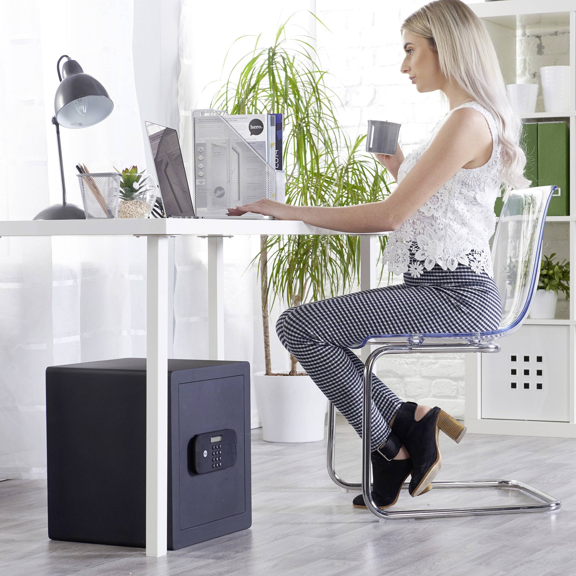 Eine Frau sitzt an einem Schreibtisch und arbeitet am Computer. Der Raum ist hell und modern eingerichtet mit Pflanzen und Dekoration.