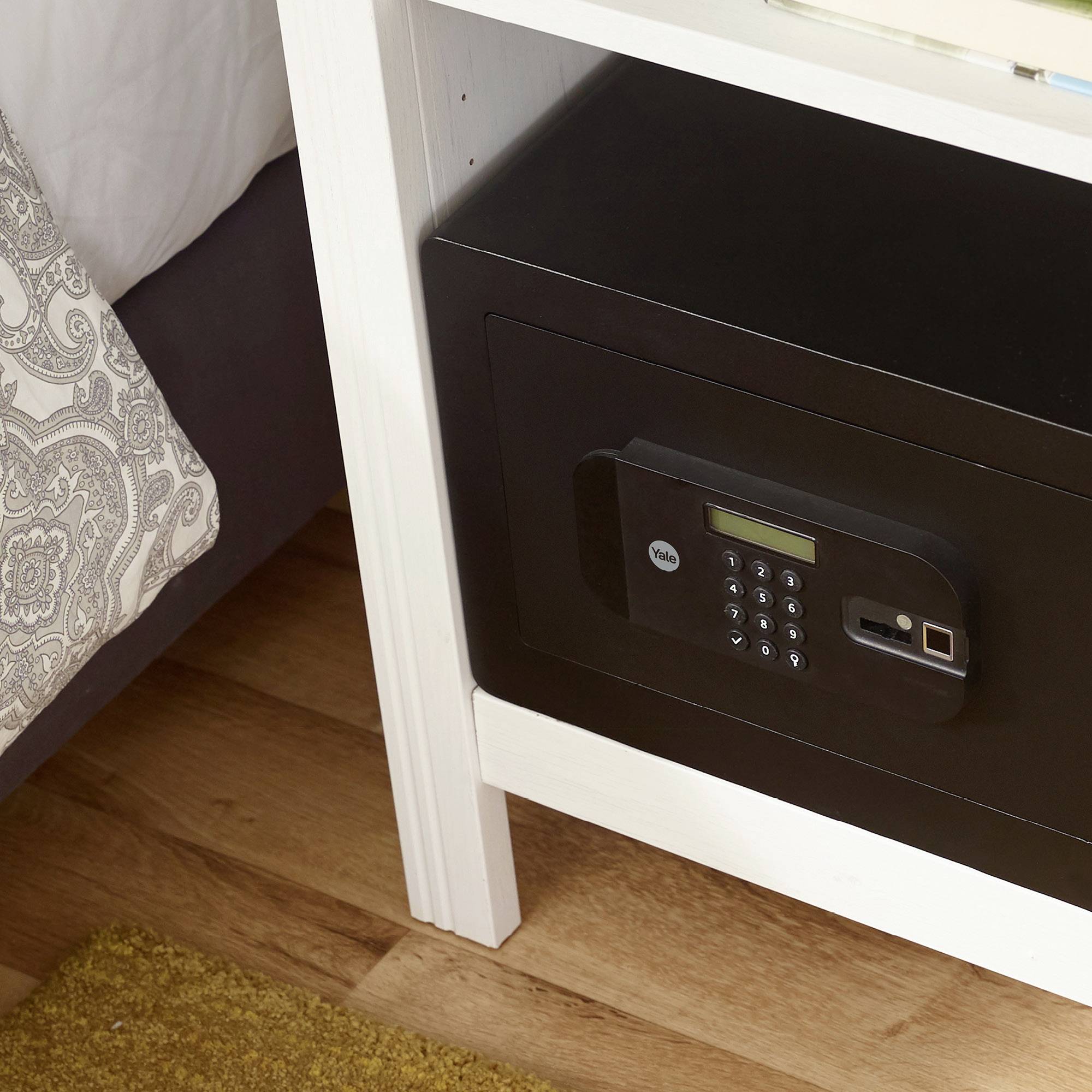 Safe eingebaut in einem Nachttisch neben einem Bett. Das Safe hat ein Tastenfeld für die Eingabe eines Codes.
