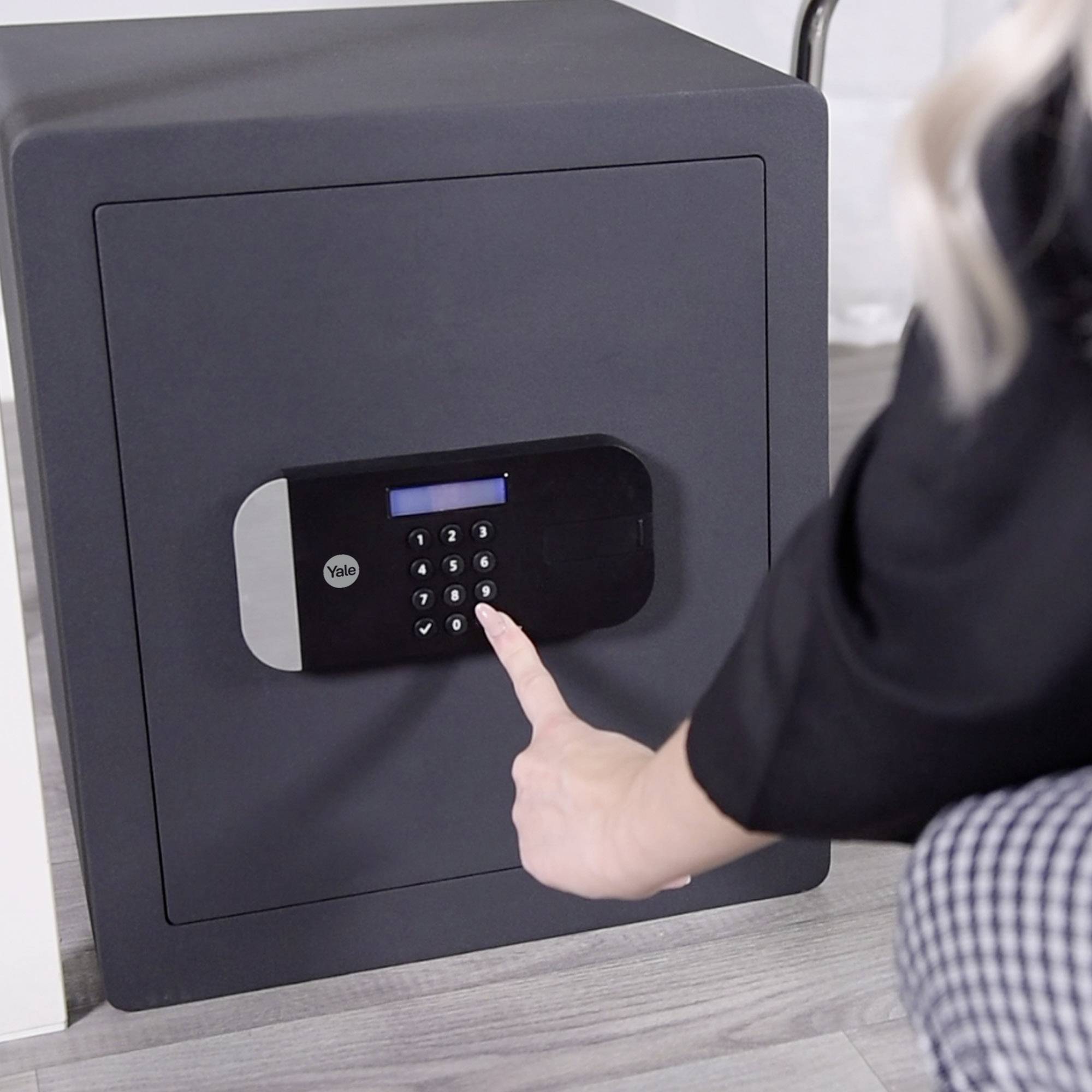 Eine Person gibt einen Code in ein elektronisches Tastenfeld eines dunkelgrauen Safes ein, um ihn zu öffnen.