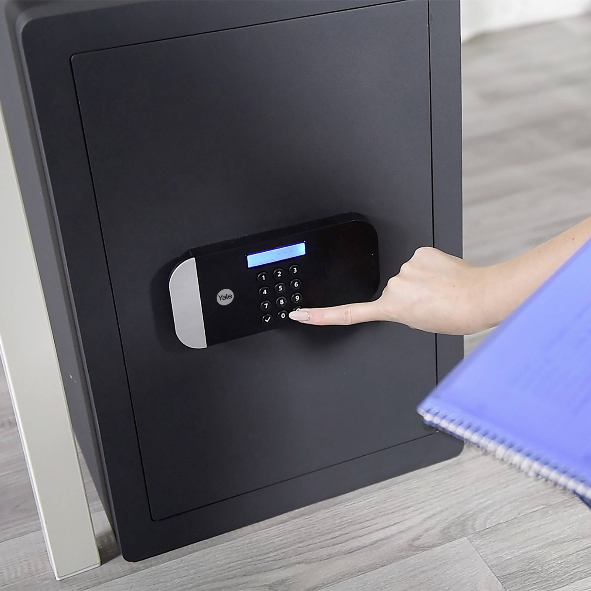 Eine Person gibt mit der rechten Hand einen Code in ein elektronisches Tresorschloss ein, während sie in der linken Hand ein Notizbuch hält.