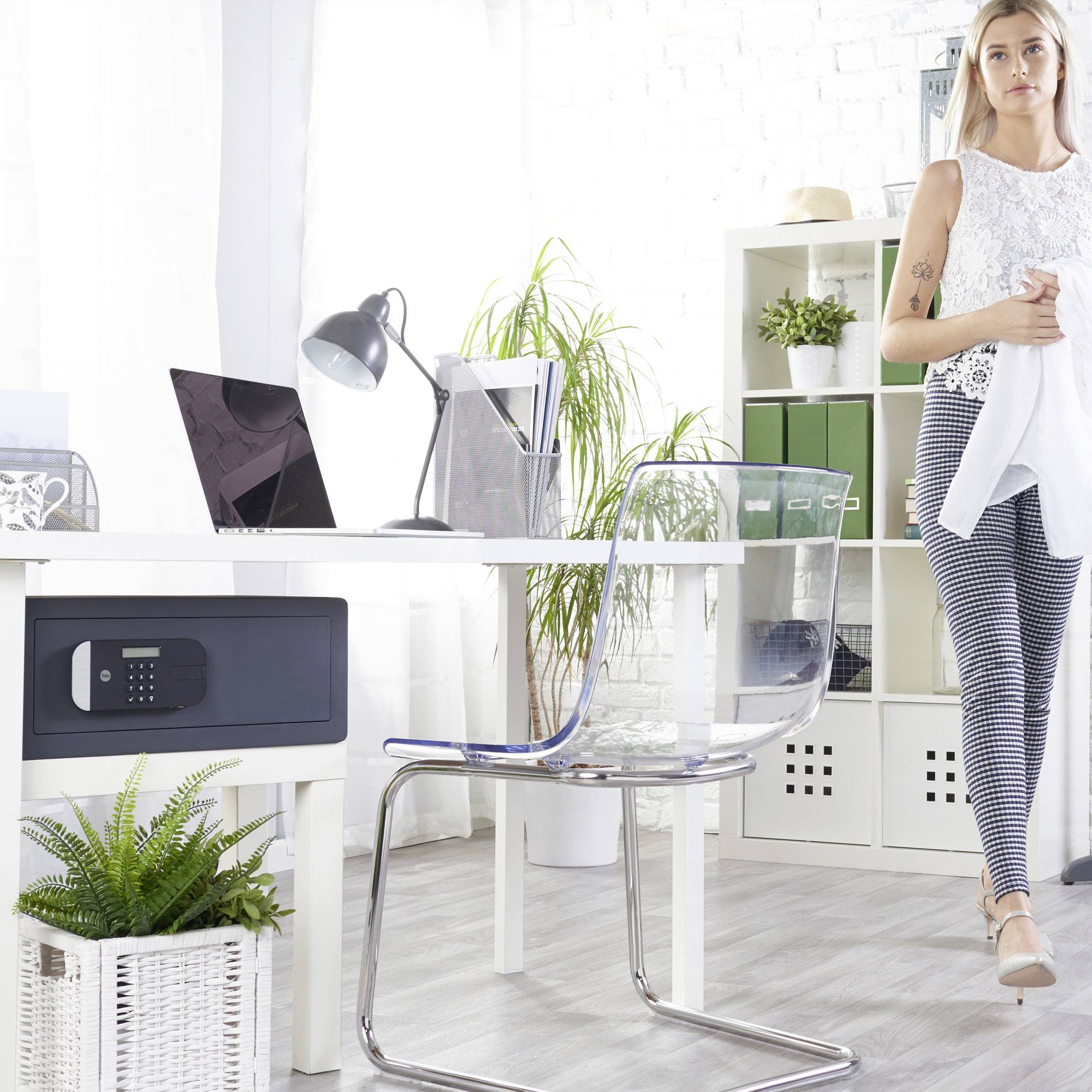 Frau in einem modernen Büro mit Pflanzen, durchsichtigen Stühlen und einem Schreibtisch. Sie hält ein weißes Kleidungsstück. Büroatmosphäre.