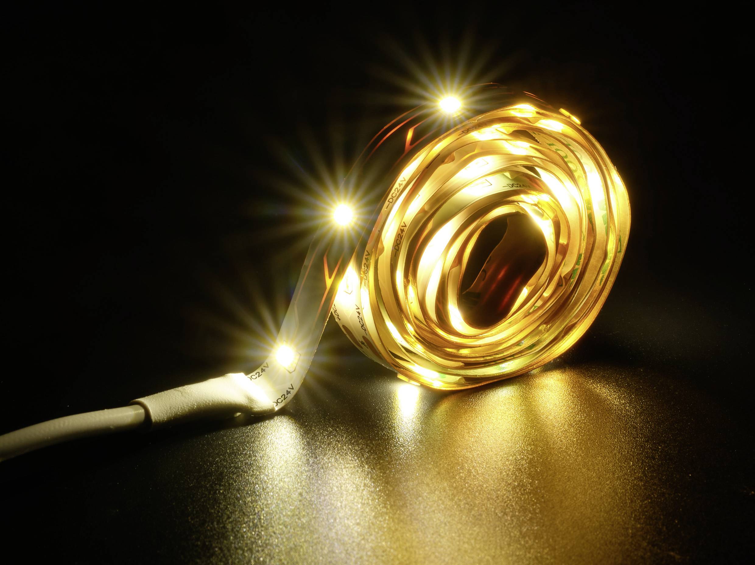 Ein leuchtendes LED-Lichtband in warmem Gelbton, aufgerollt auf einer dunklen Oberfläche. Strahlt ein sanftes, intensives Licht aus.