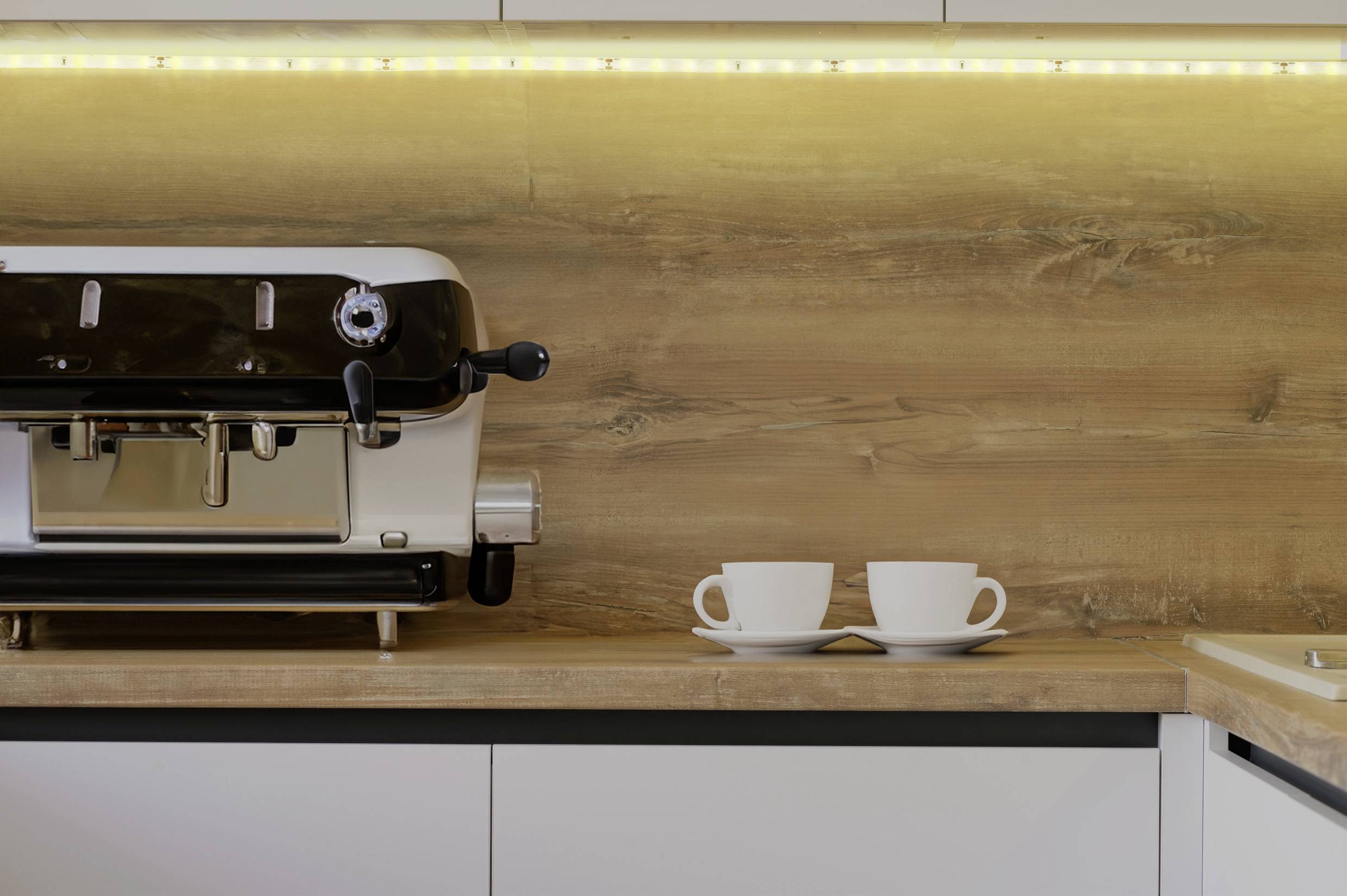 Eine Kaffeemaschine auf einer Arbeitsplatte neben zwei leeren Tassen, umgeben von warmem Hintergrundlicht.