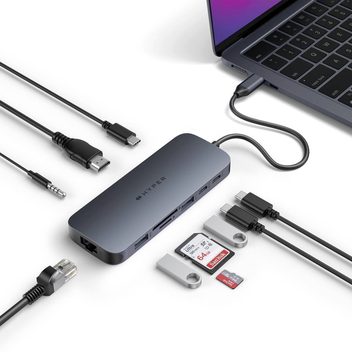 Ein Laptop ist an ein USB-C-Hub angeschlossen, das mehrere Anschlüsse bietet: HDMI, USB, Ethernet, SD-Kartenleser und Audioanschluss. Adapter und Kabel sind daneben platziert.