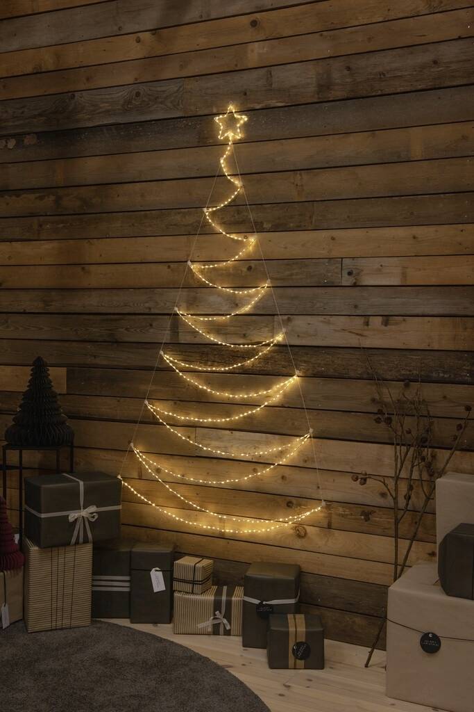 Lichterketten in Form eines Weihnachtsbaums an einer Holzwand, umgeben von Geschenken.