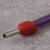 Ein violettes Kabel mit rotem Kunststoffschutz umgibt eine Metallsteckverbindung auf einem grauen Hintergrund.