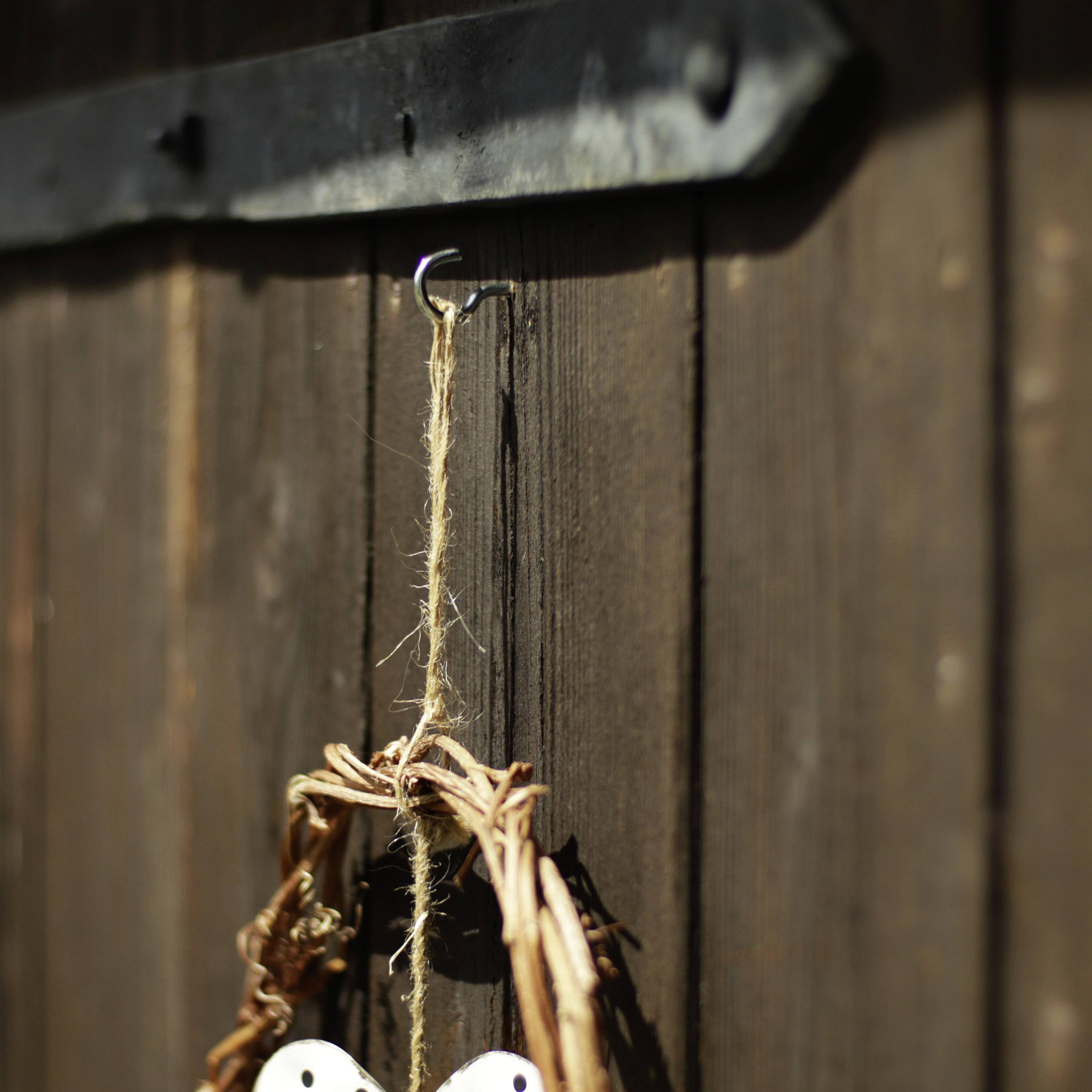 Holzwand mit aufgehängtem Weidenkranz, der an einem Haken befestigt ist, in natürlichem Licht hervorgehoben.