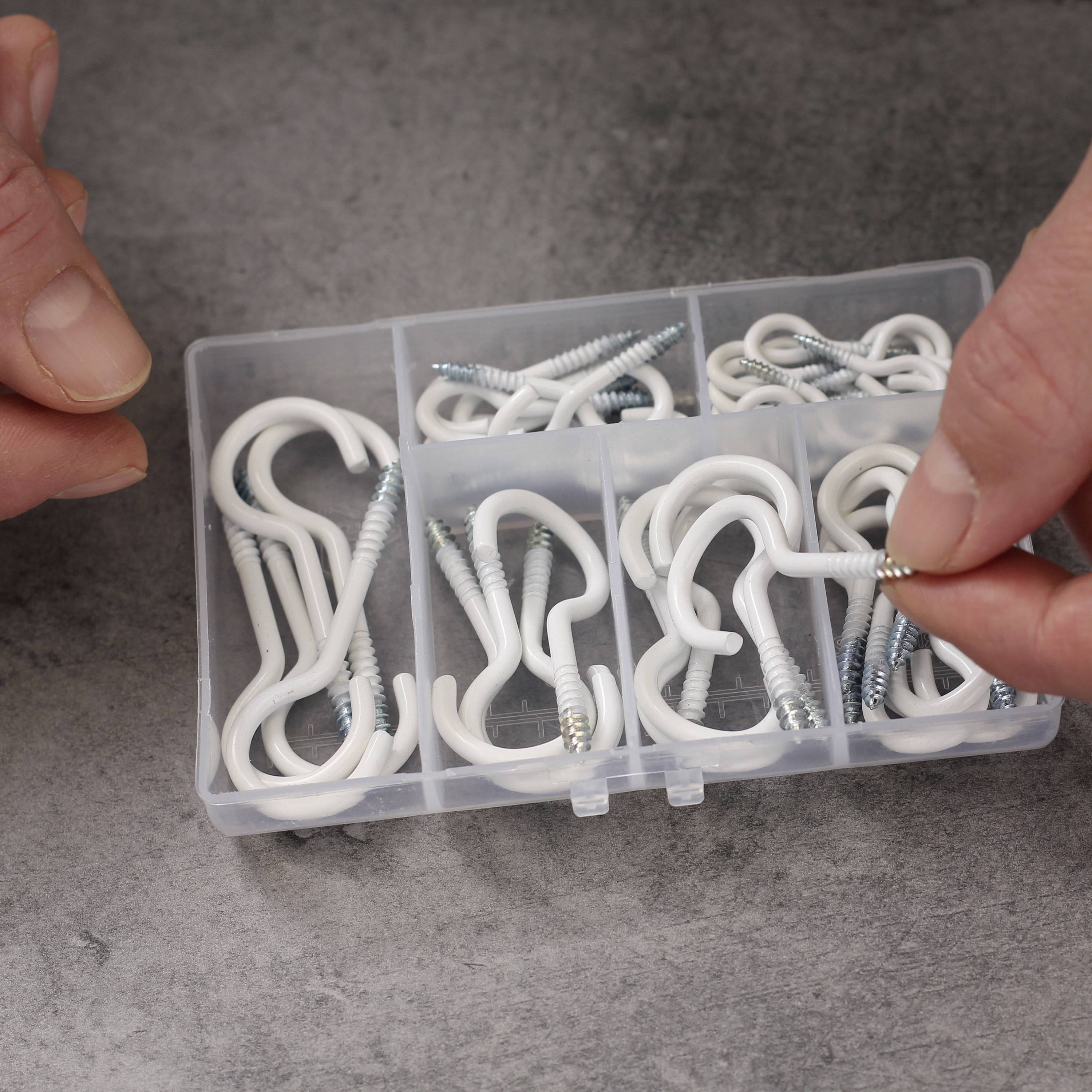 Eine offene Plastikbox mit verschiedenen Häkchen und Schrauben. Zwei Hände halten eine kleine Schraube.