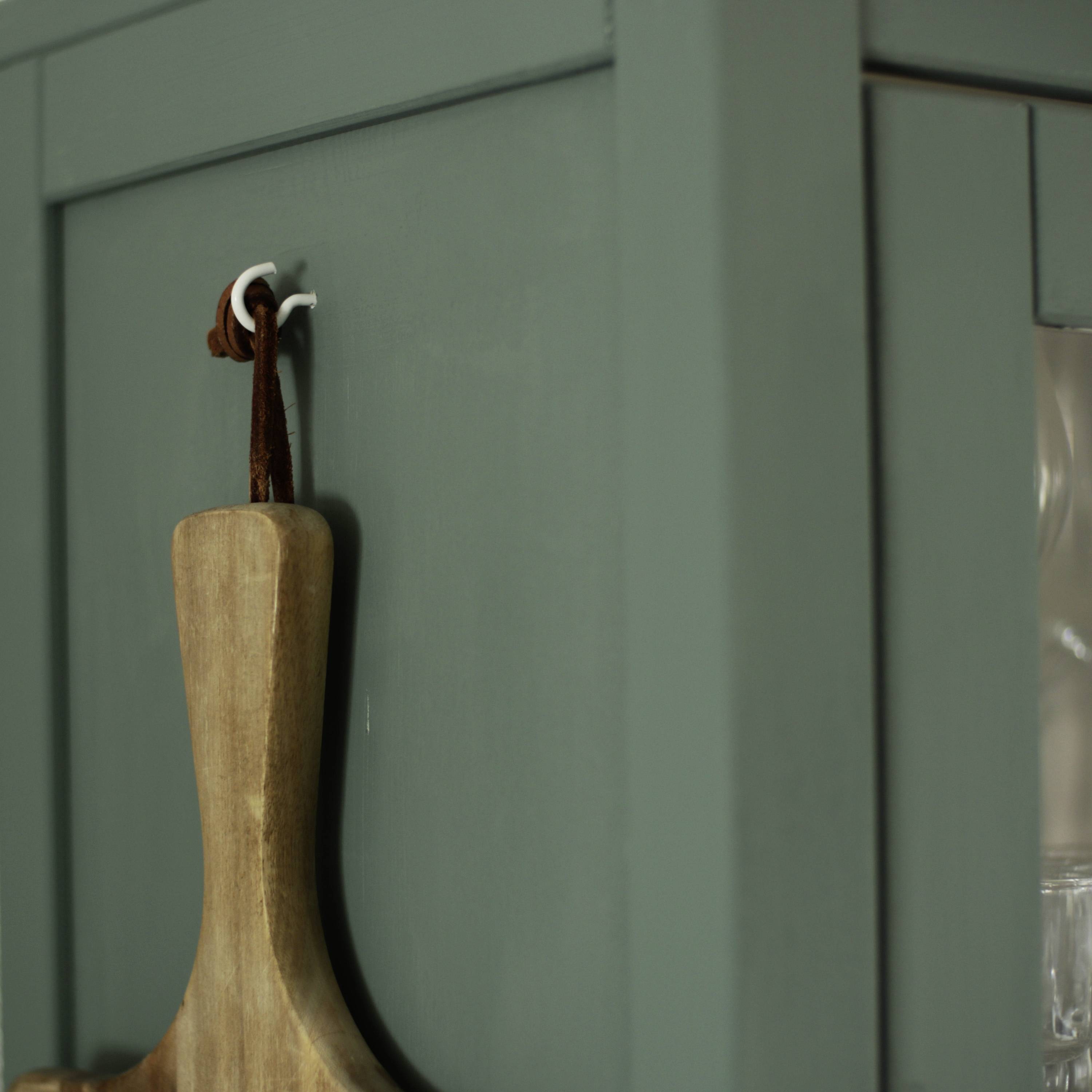 Ein Holzbrett hängt an einem Haken an einer grauen Wand.