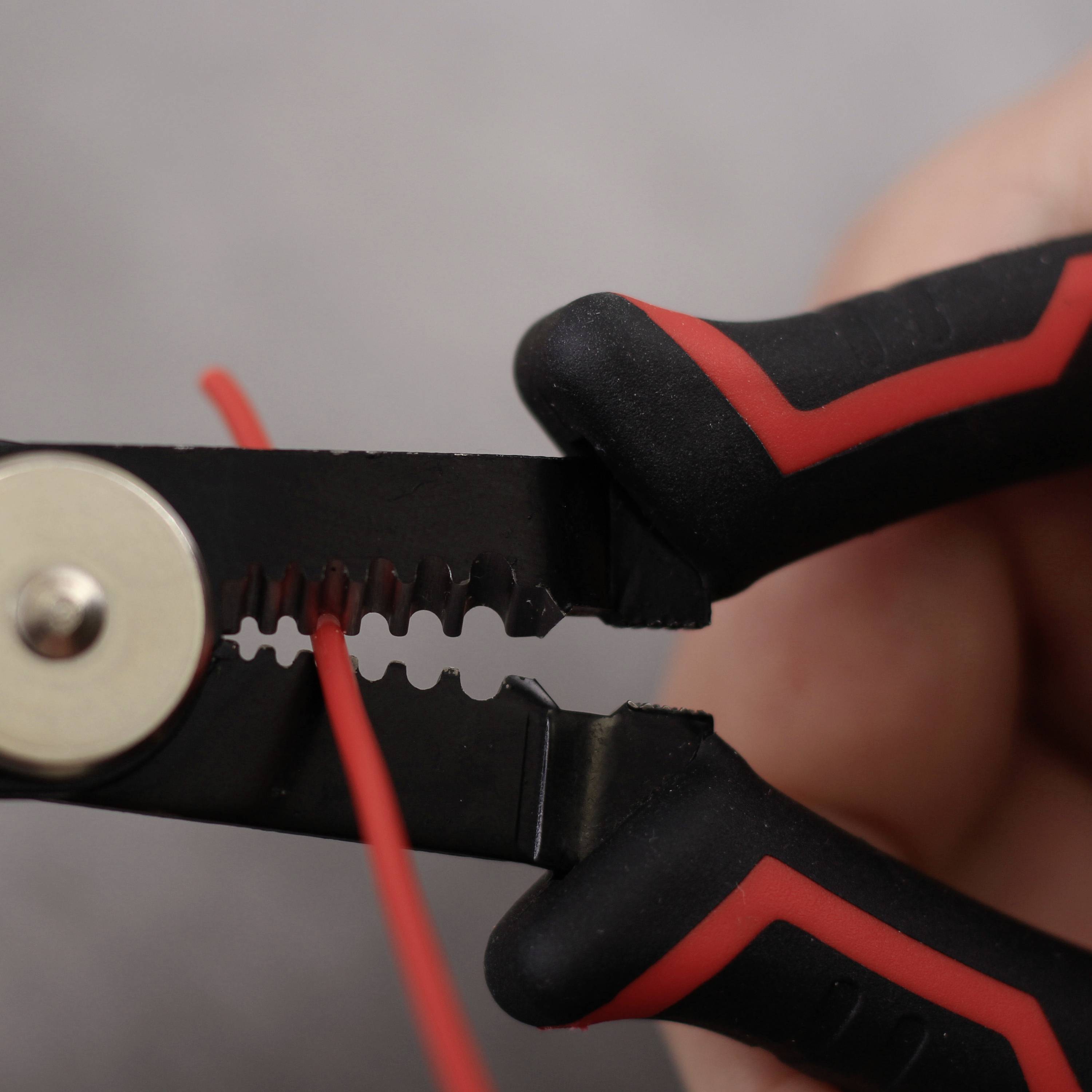 Eine Hand hält eine schwarze und rote Abisolierzange mit einem Kupferdraht dazwischen.