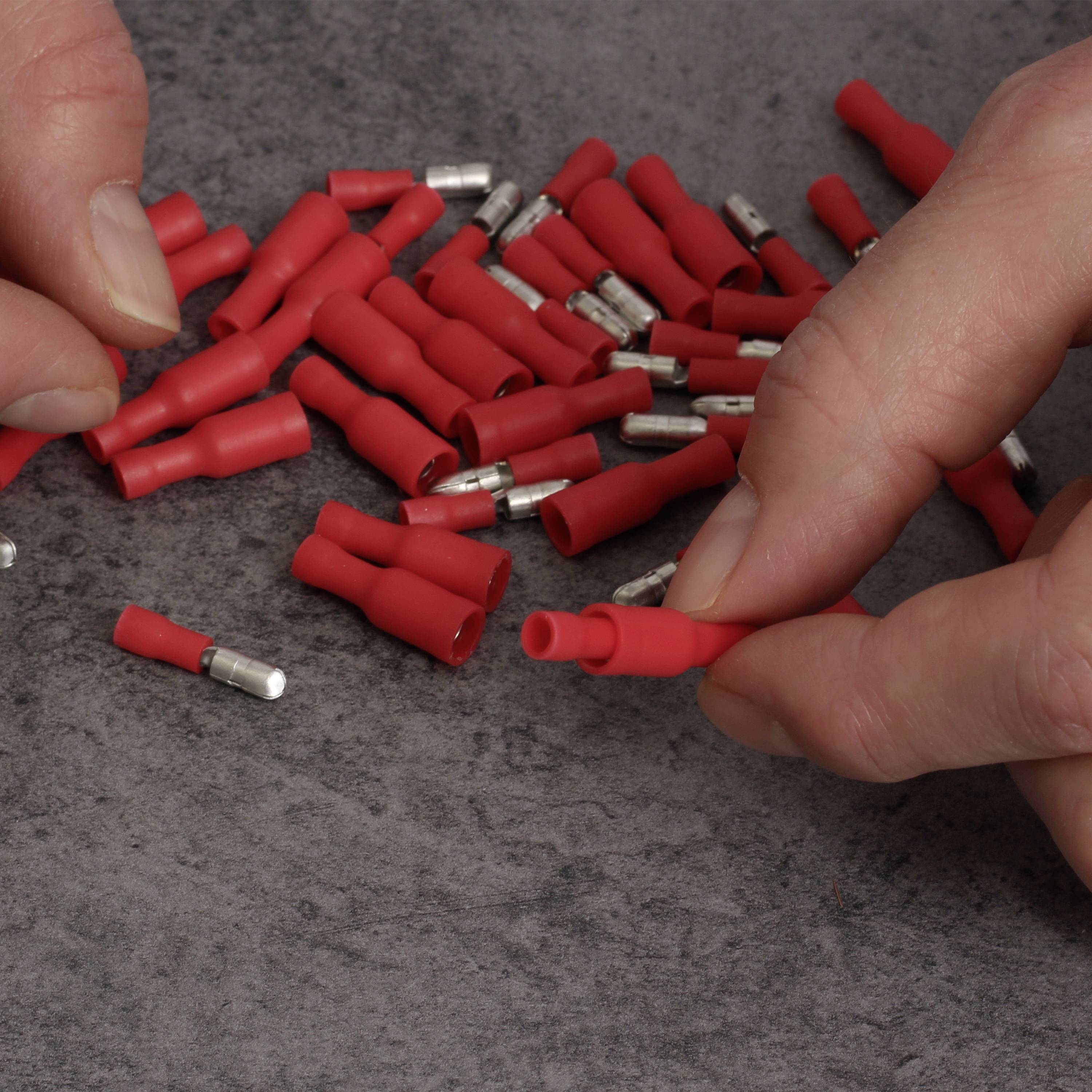 Eine Person hält einen roten elektrischen Steckverbinder. Viele weitere rote Steckverbinder liegen auf einem grauen Tisch.