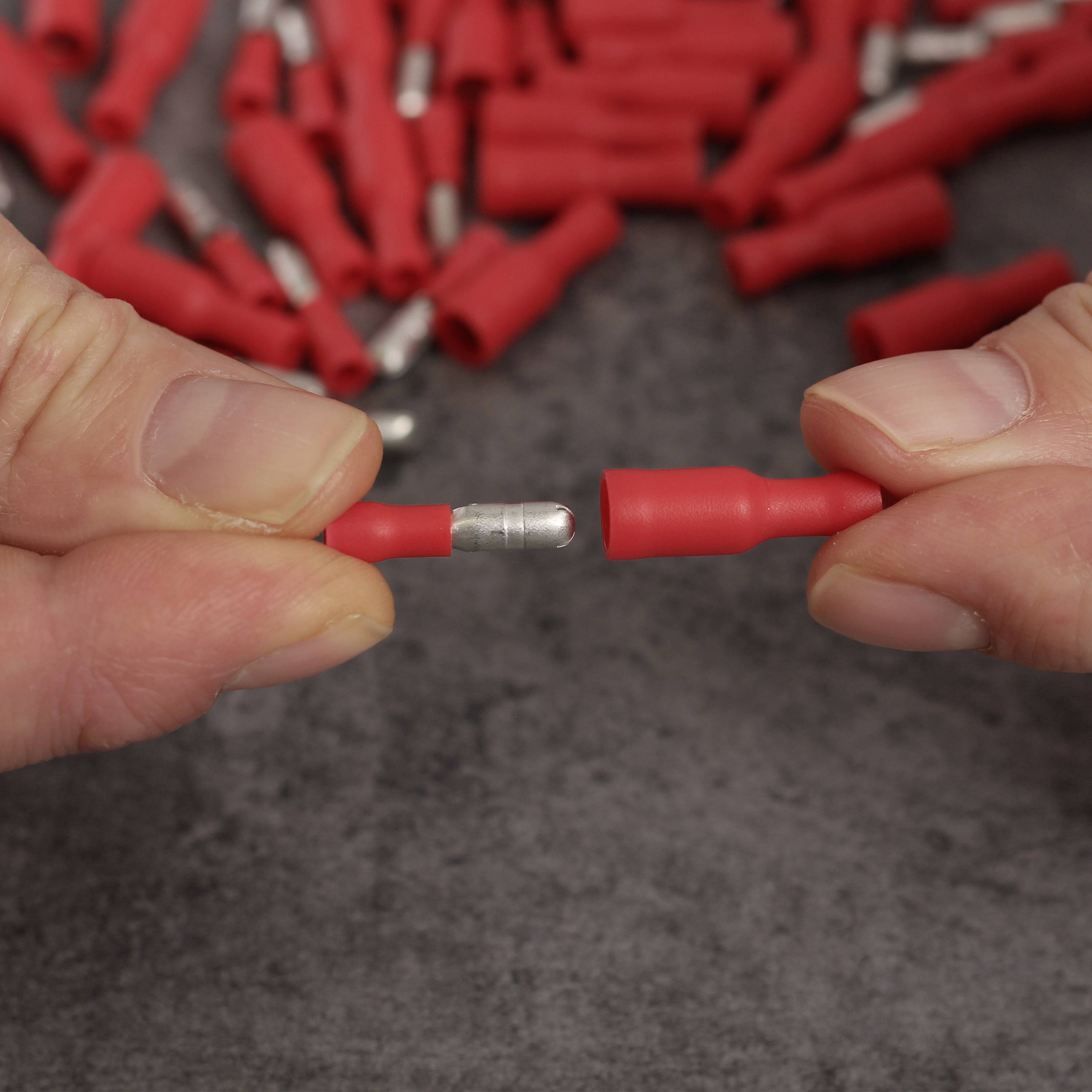 Eine Person hält zwei rote Steckverbinder in den Händen. Im Hintergrund sind weitere Steckverbinder auf einem grauen Untergrund zu sehen.