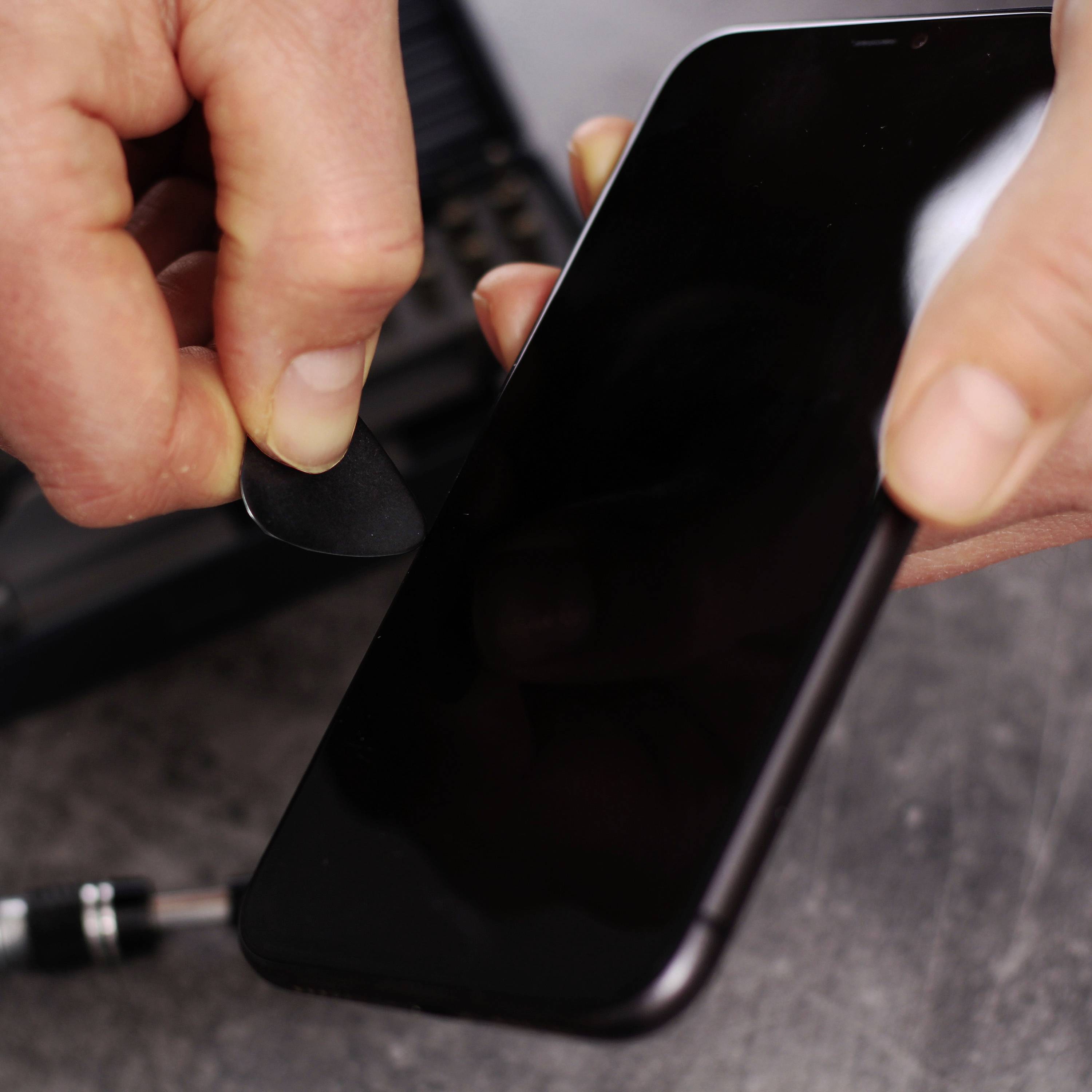 Eine Person benutzt ein kleines Werkzeug, um das Display eines Smartphones zu öffnen. Konzentration auf Reparatur oder Wartung.