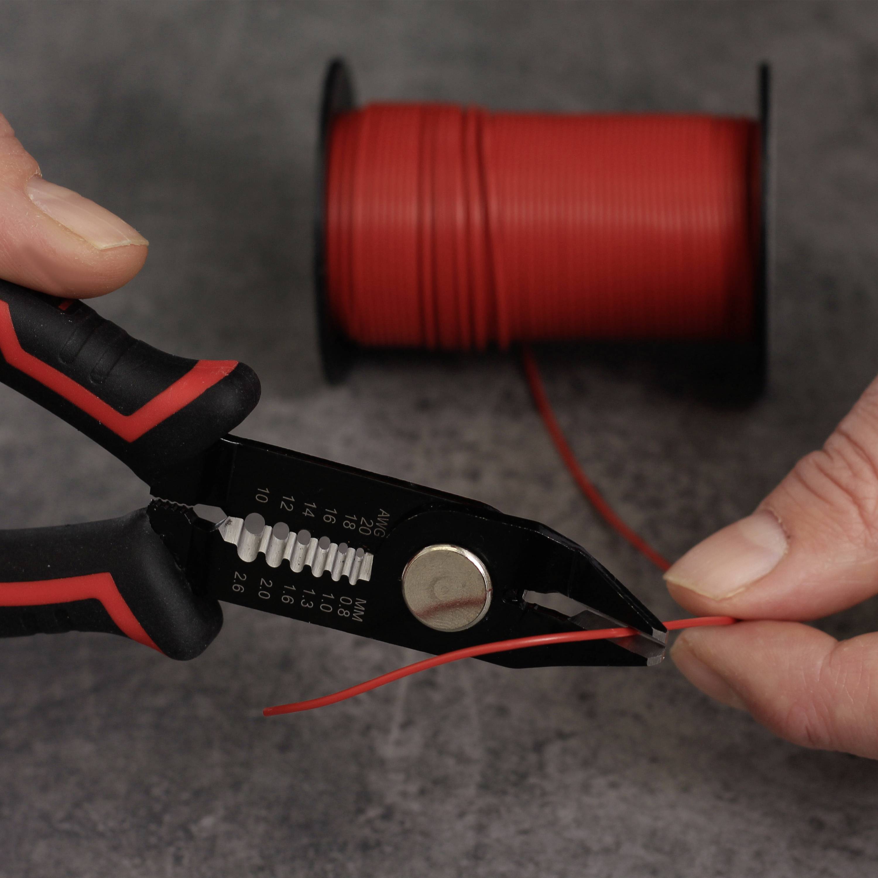 Hände schneiden mit einer Zange ein rotes Kabel von einer Rolle.