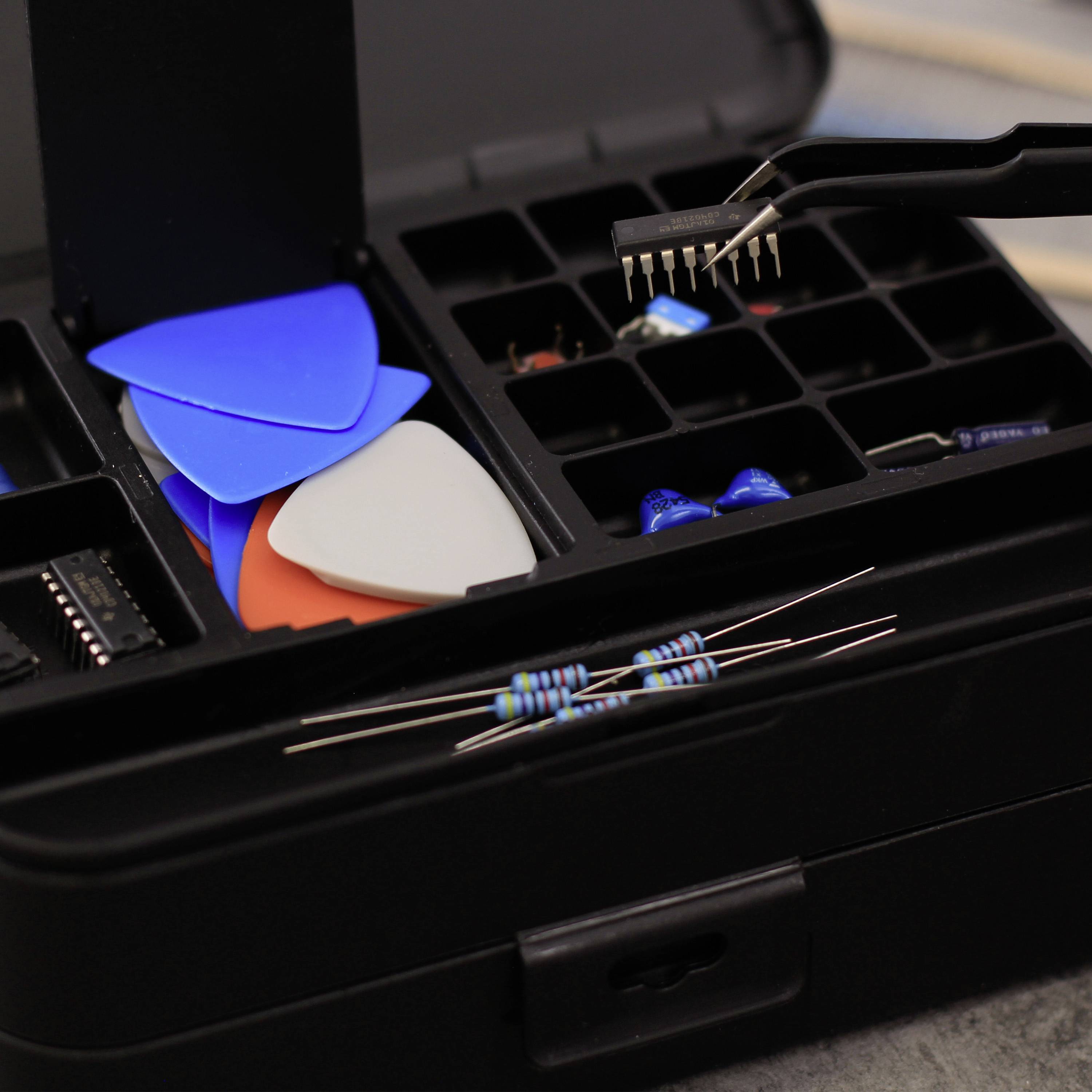 Eine offene Box mit Sortierfächern, gefüllt mit blauen und orangefarbenen Plektren. Im Vordergrund liegen zwei Widerstände.