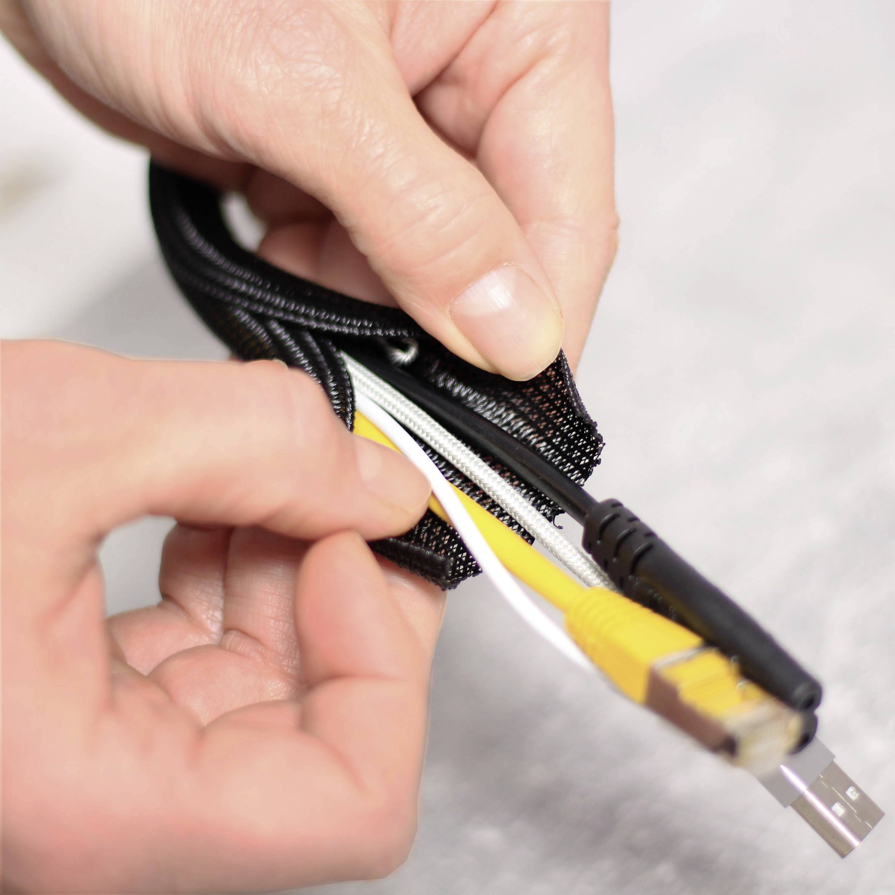 Ein paar Hände hält mehrere Kabel, die durch eine schwarze Kabel-Hülle gebündelt werden. Die Kabel haben USB- und LAN-Stecker.