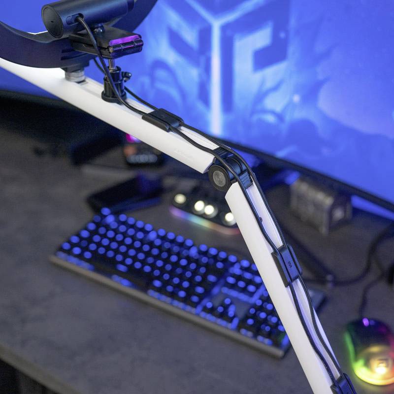 Eine Gaming-Setup mit beleuchteter Tastatur und Maus, einem großen Monitor im Hintergrund und einem befestigten Mikrofonarm im Vordergrund.