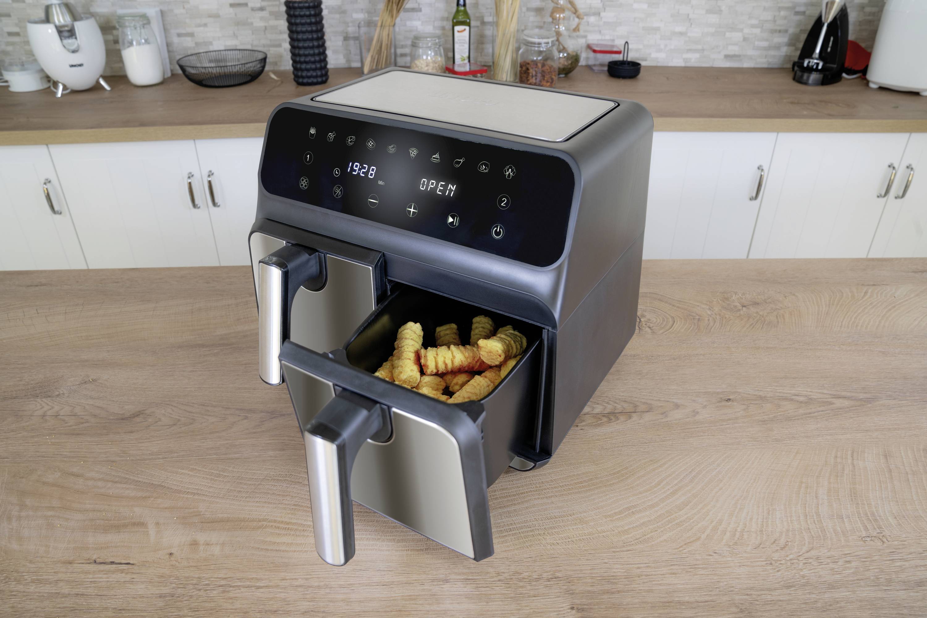 Eine Heißluftfritteuse auf einer Küchenarbeitsplatte mit einer geöffneten Schublade, die Pommes frites enthält.