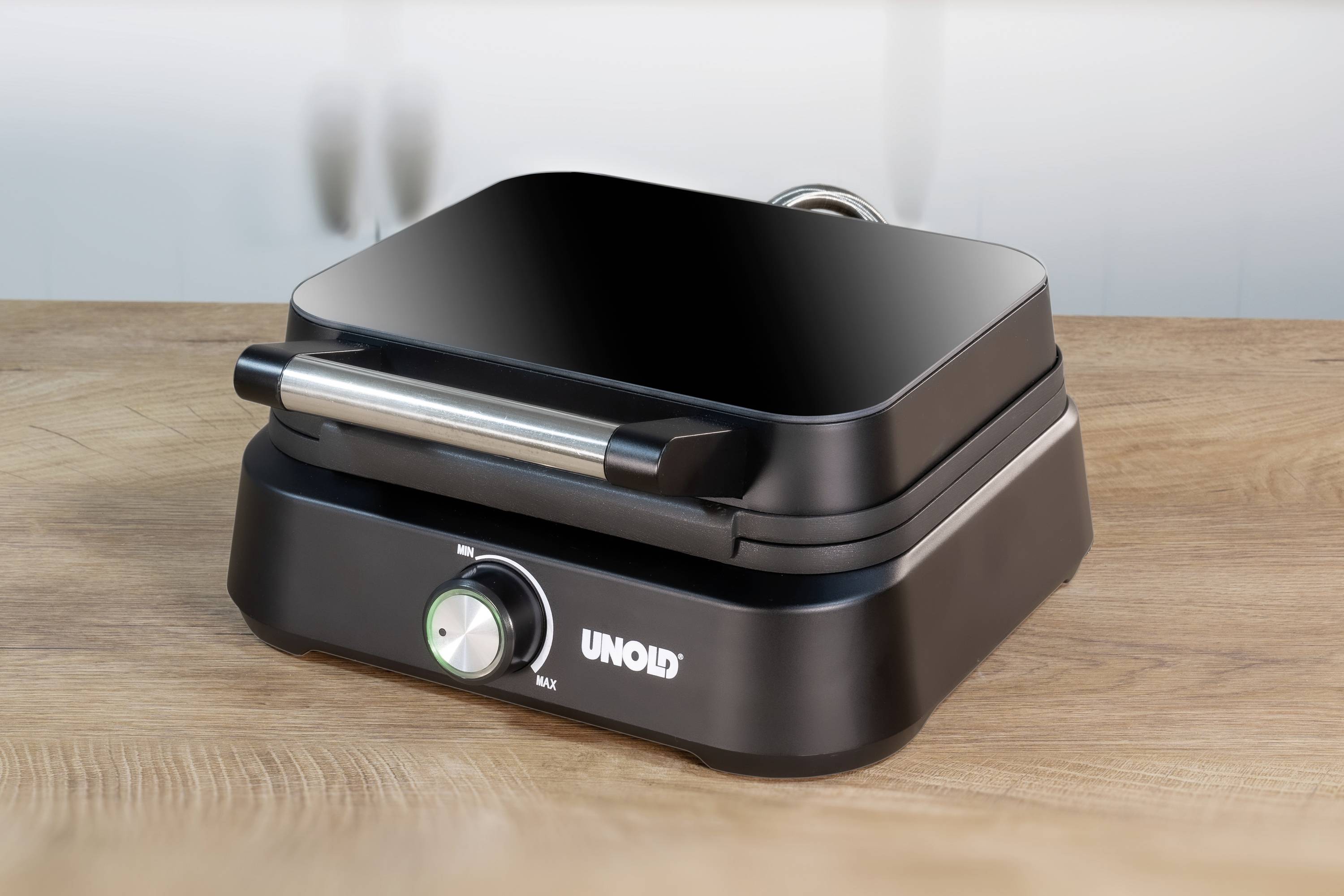 Schwarzer Kontaktgrill mit silbernem Griff und Drehknopf auf holzähnlicher Oberfläche.