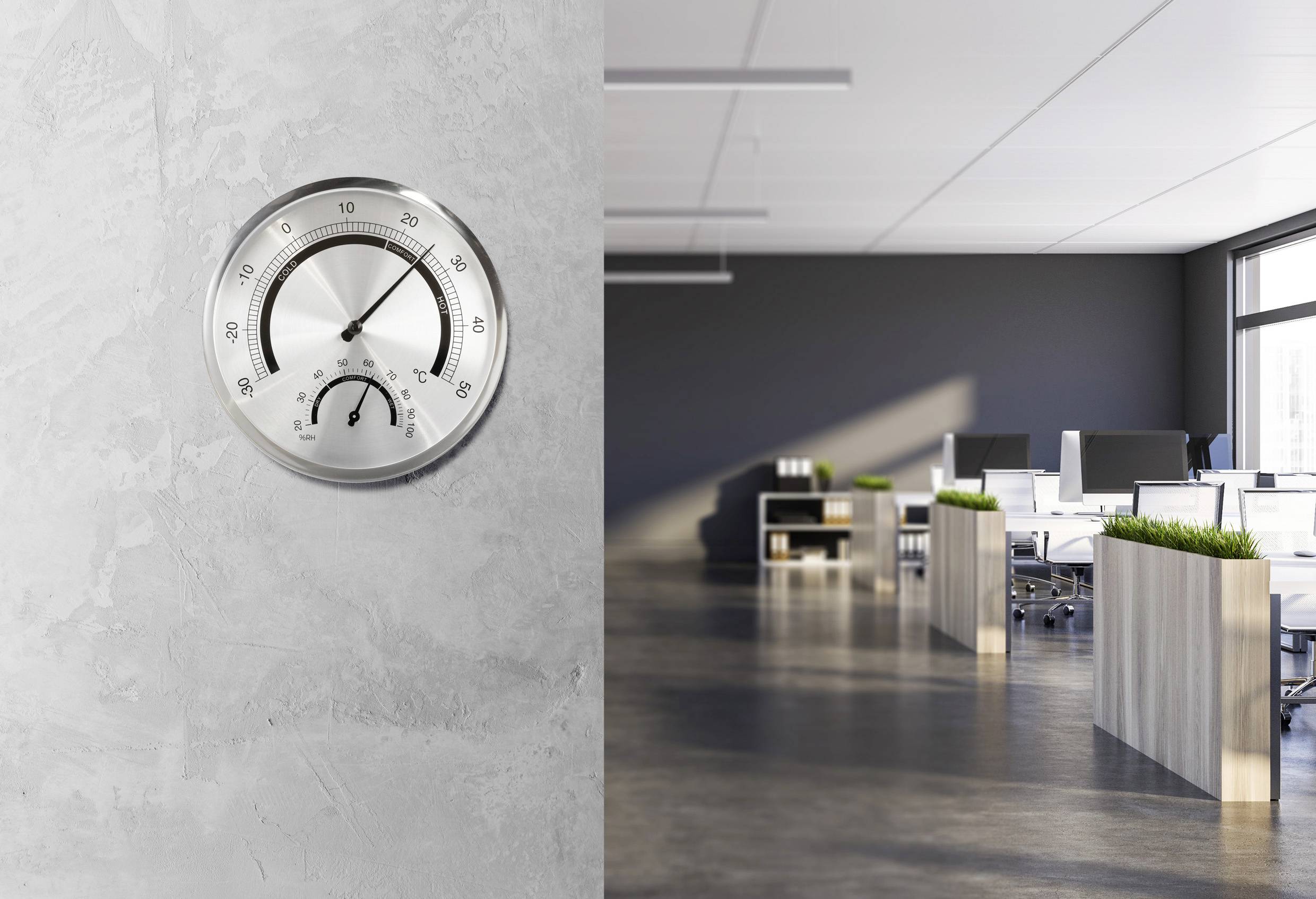 Helles Büro mit modernen Schreibtischen und Pflanzen. Ein silbernes Thermometer an der Wand zeigt Raumtemperatur und Luftfeuchtigkeit an.