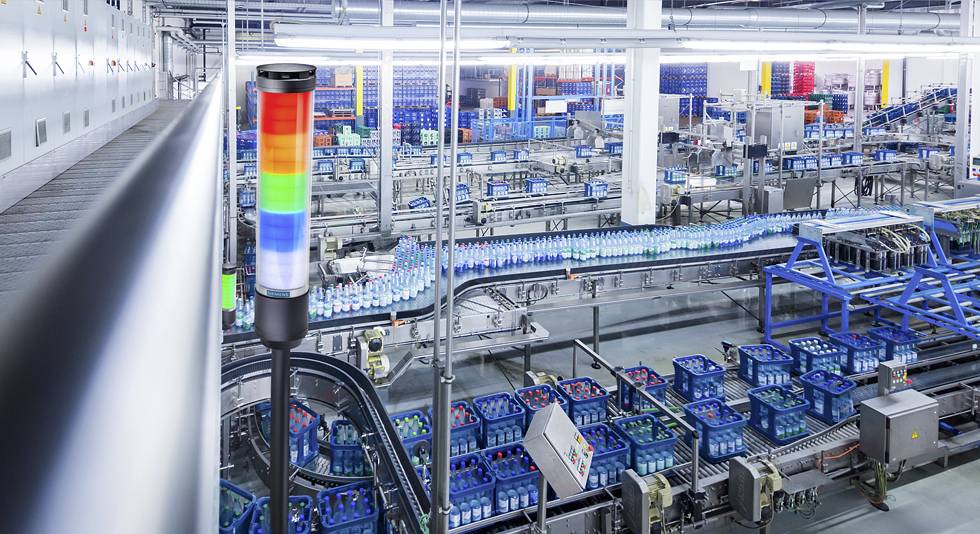 Eine automatisierte Getränkefabrik mit Fließbändern voller Flaschen. Ein mehrfarbiges Warnlicht signalisiert den Produktionsstatus.
