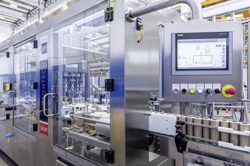 Eine moderne Verpackungsmaschine in einer Fabrik, mit einem Bedienfeld rechts. Im Hintergrund sind Industrieelemente zu sehen.