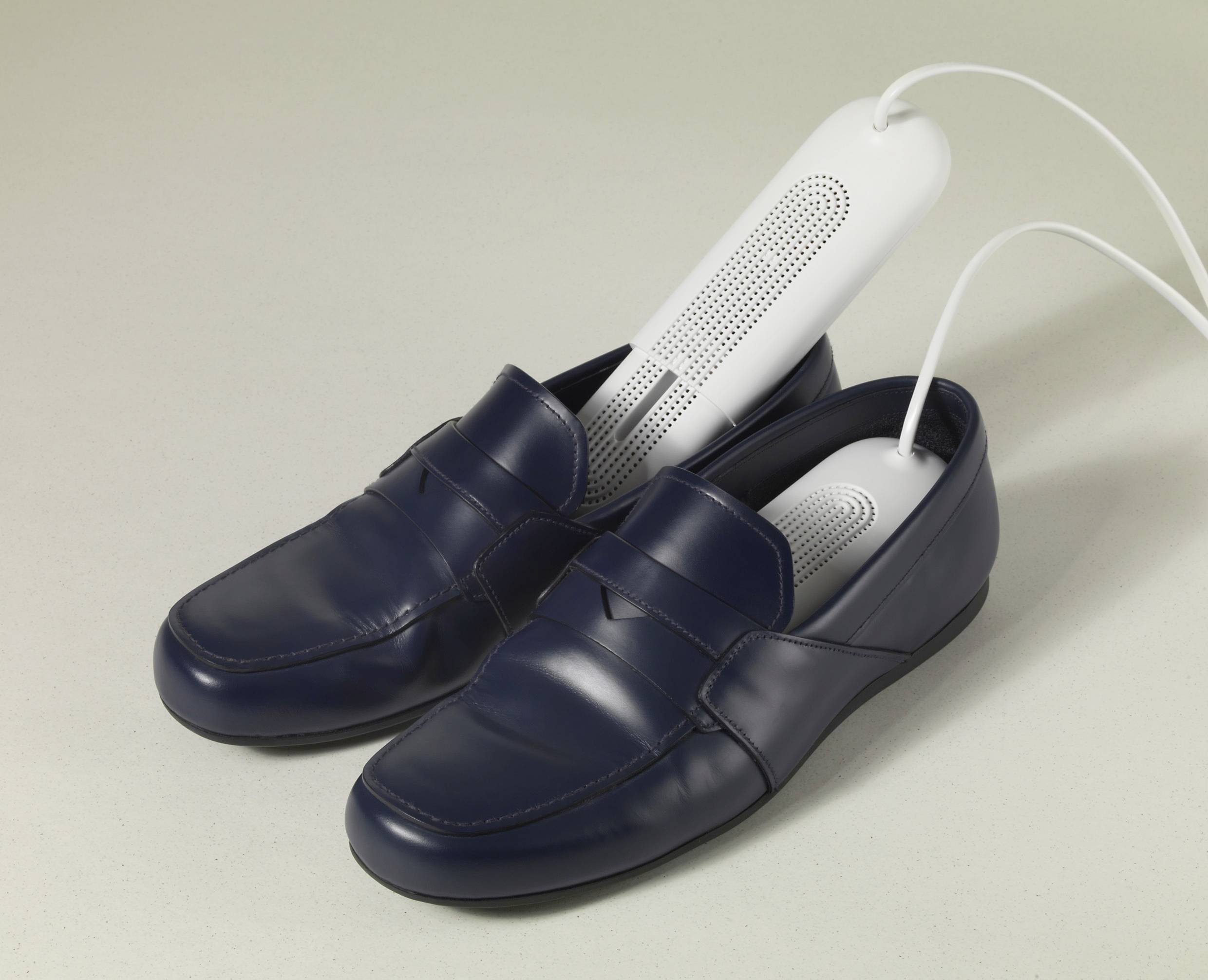 Dunkelblaue Loafers mit eingesetzten weißen Schuhheizern, die über Kabel verbunden sind. Die Heizer sind zu Reinigungszwecken eingefügt.