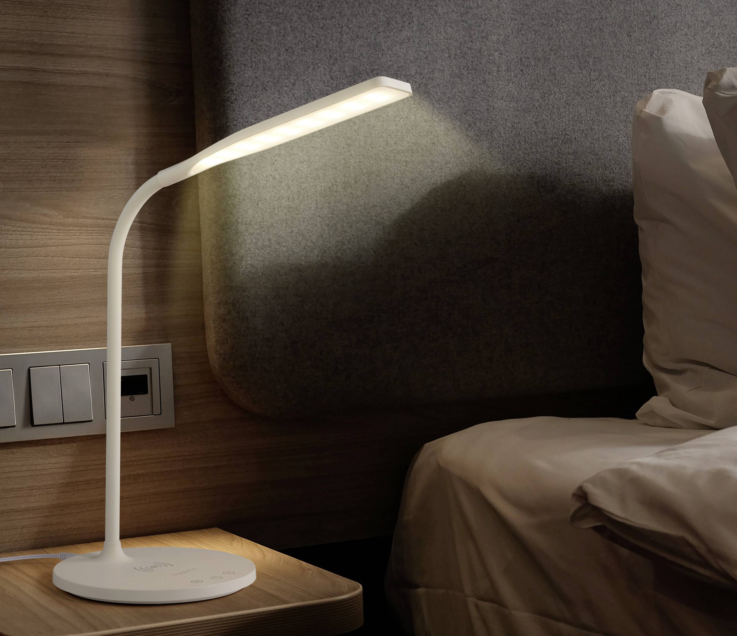Weiße Tischlampe mit flexiblem Hals leuchtet auf einem Nachttisch neben einem Bett, eingebettet in eine gemütliche Schlafzimmerumgebung.