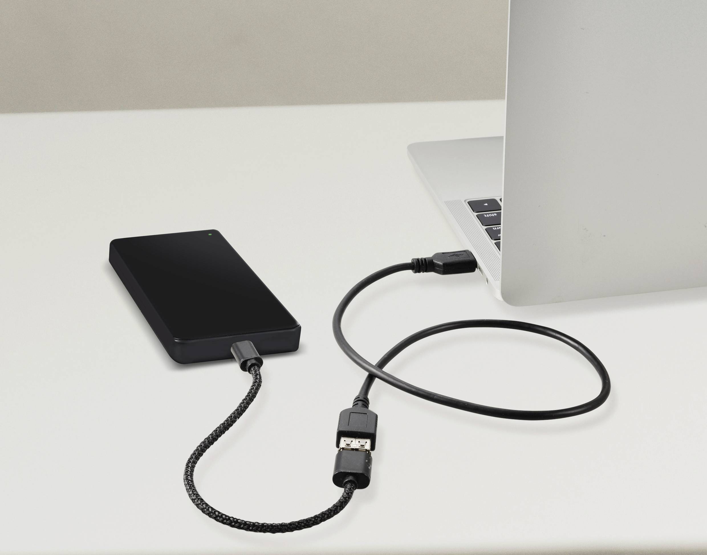 Ein externer schwarzer Festplattenspeicher ist mit einem Laptop verbunden, der auf einem weißen Tisch steht.