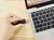 Hand hält ein HDMI-Kabel neben einem Laptop. Der Laptop hat eine geöffnete Tastatur und einen Bildschirm mit Naturhintergrund.