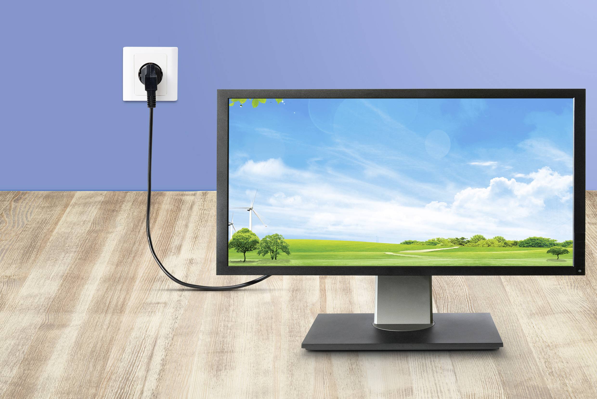 Ein Monitor zeigt eine Landschaft mit Windmühle und Bäumen, verbunden mit einer Steckdose, symbolisiert Energieverbrauch oder Nachhaltigkeit.