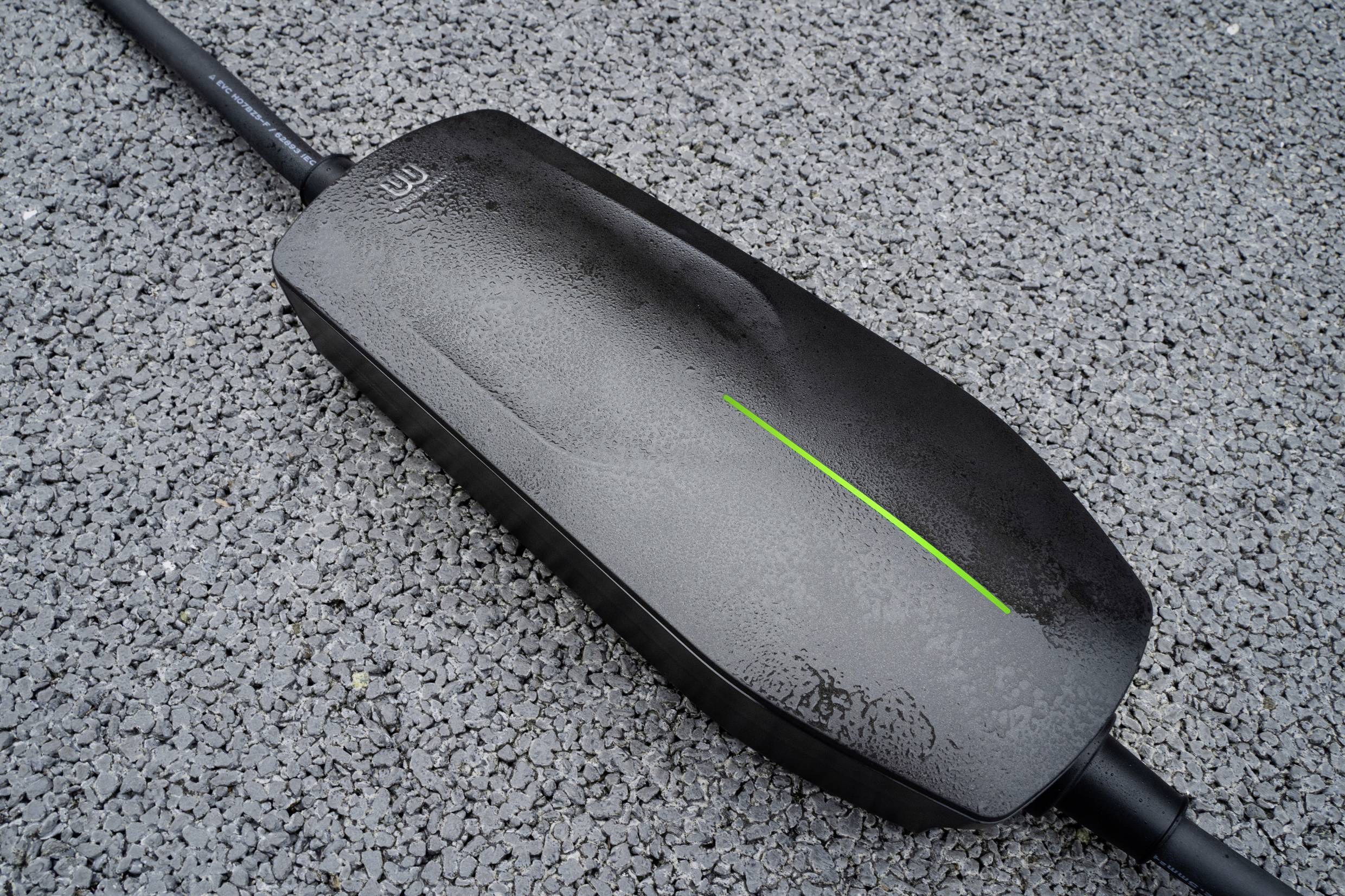 Ein schwarzer Ladegerät auf Asphalt zeigt einen grünen Lichtstreifen.
