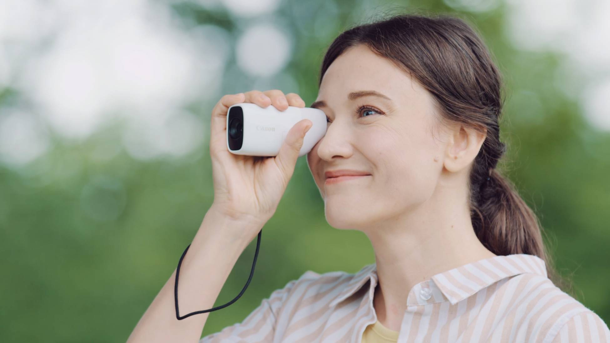 Eine Frau schaut durch ein kleines tragbares Monokular, umgeben von unscharfem grünem Hintergrund, vermutlich in einem Park oder Wald.