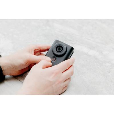 Person hält eine kleine, schwarze Kamera in den Händen auf einer grauen, marmorierten Oberfläche.