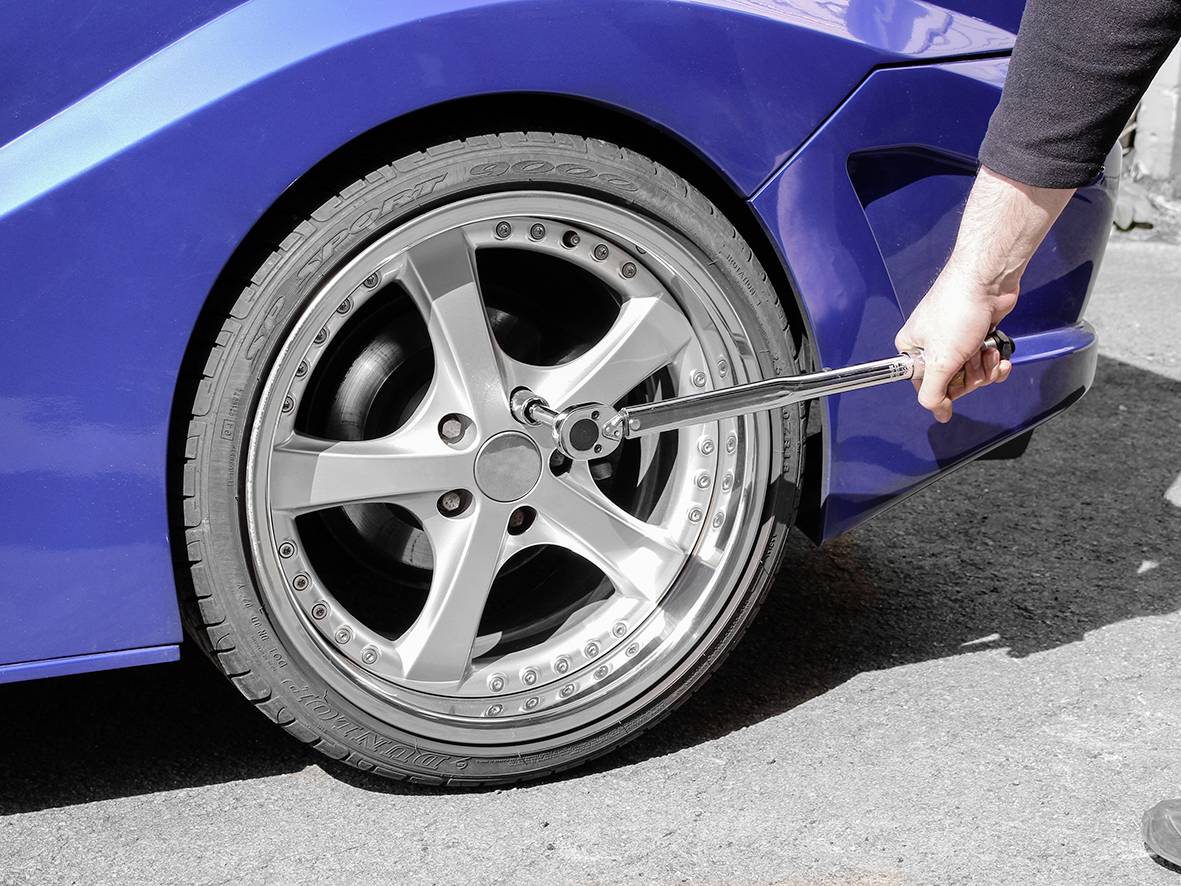 Eine Person wechselt mit einem Werkzeug den Reifen eines blauen Autos. Der Fokus liegt auf dem Autoreifen und dem Werkzeug.