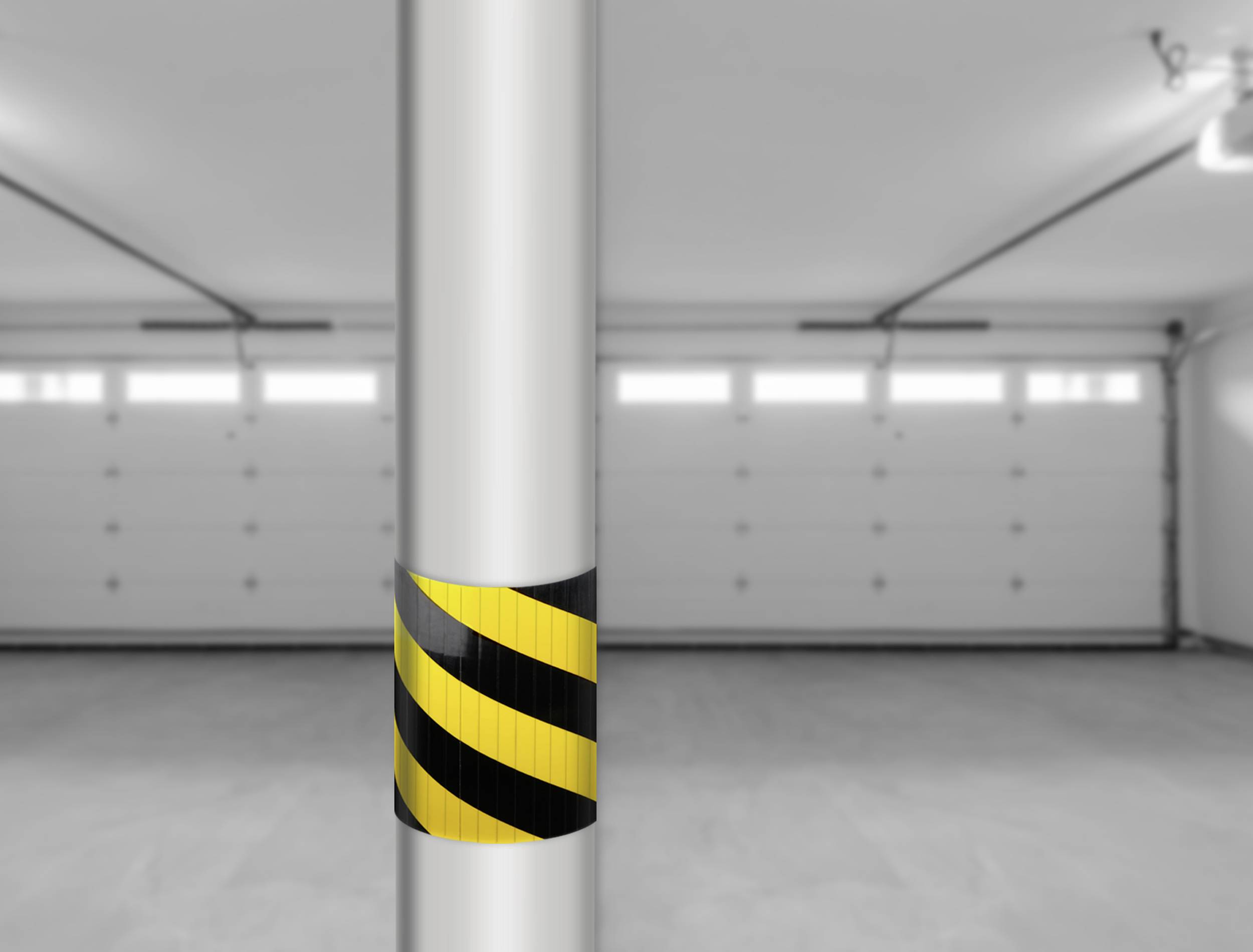 Eine leere Garage mit einem zentralen Pfeiler, der schwarz-gelb gestreift ist. Die Garage hat geschlossene, weiße Tore im Hintergrund.